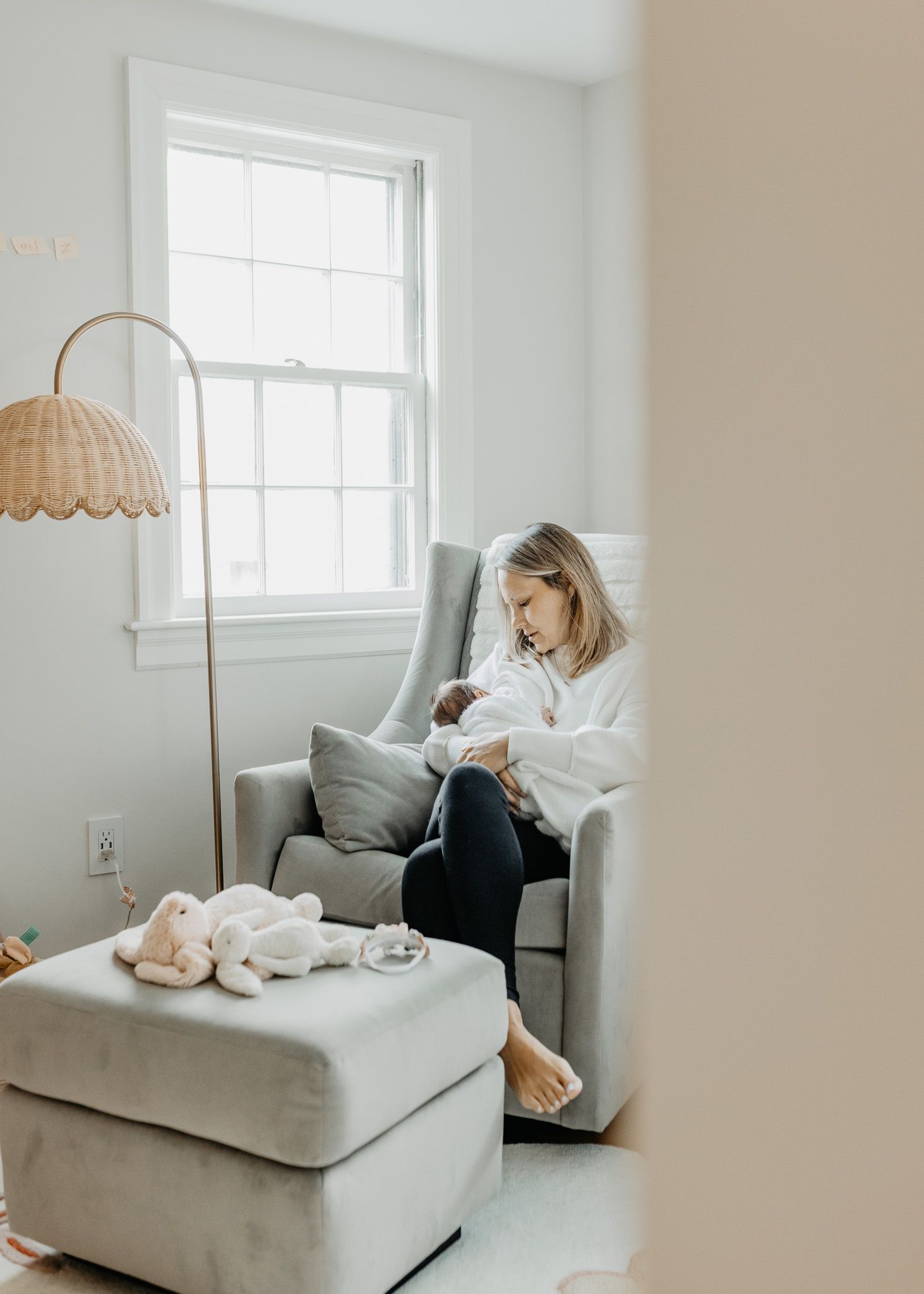 Cozy nursery scene with person in white robe reading in armchair next to window.