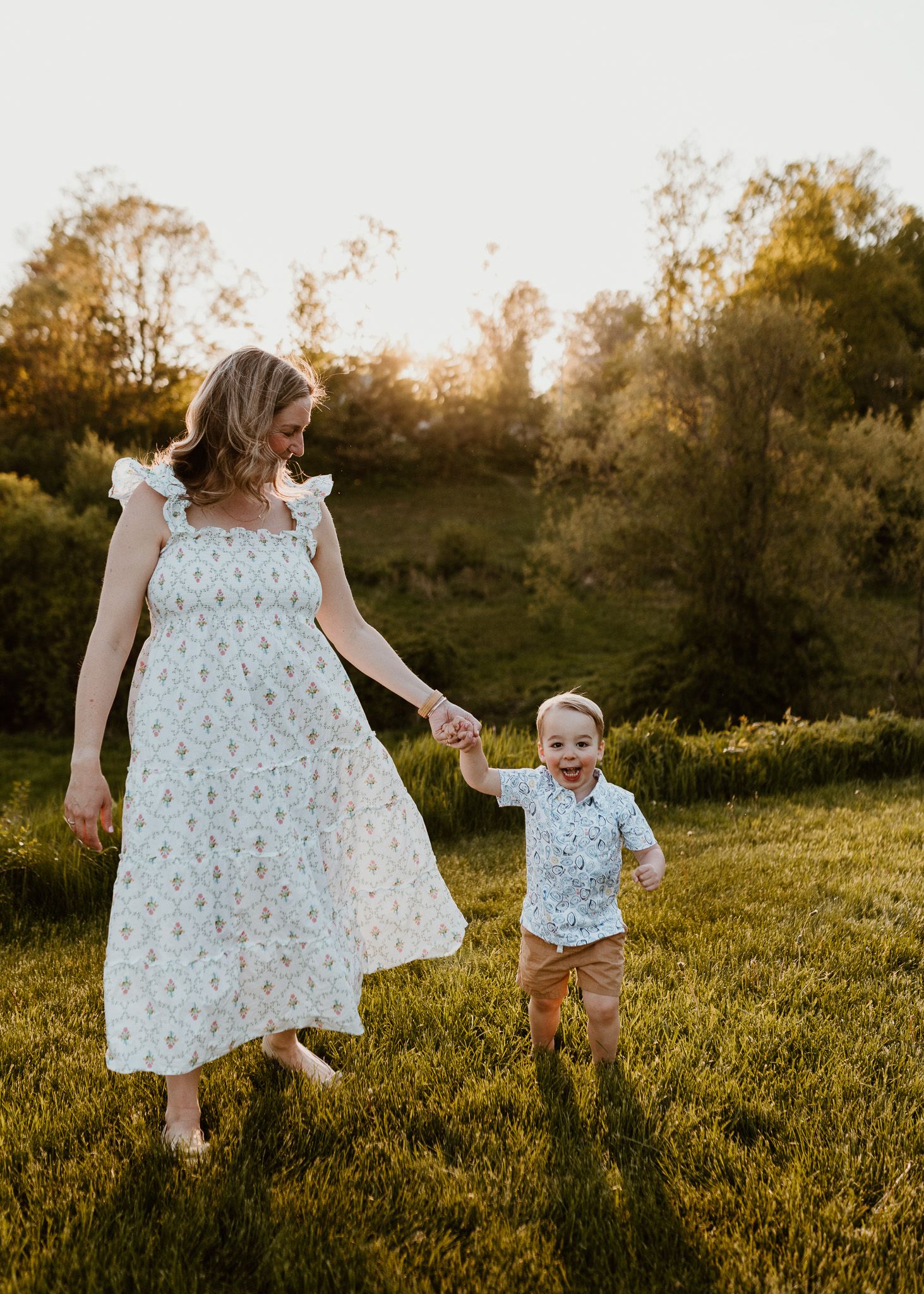 Mother and child holding hands while dancing in a sunlit meadow at golden hour.