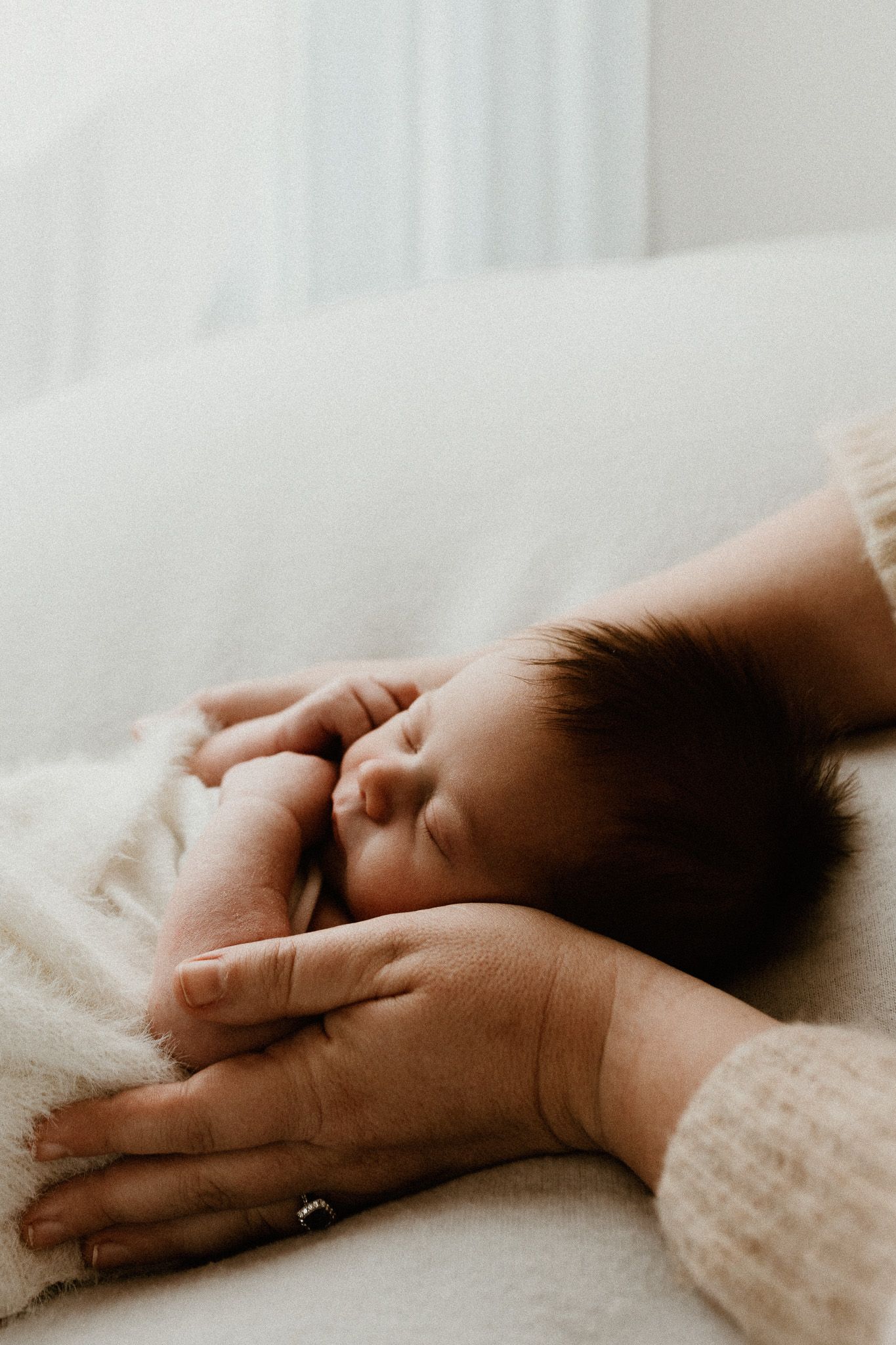 Close-up of sleeping newborn baby's face with gentle hands nearby.