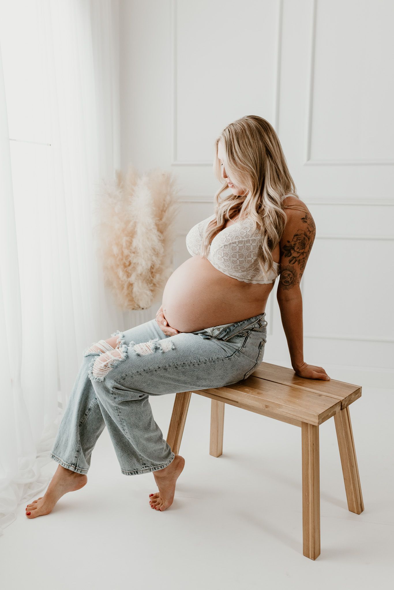 Maternity photo sequence showing pregnant woman in jeans sitting on wooden bench against white wall.