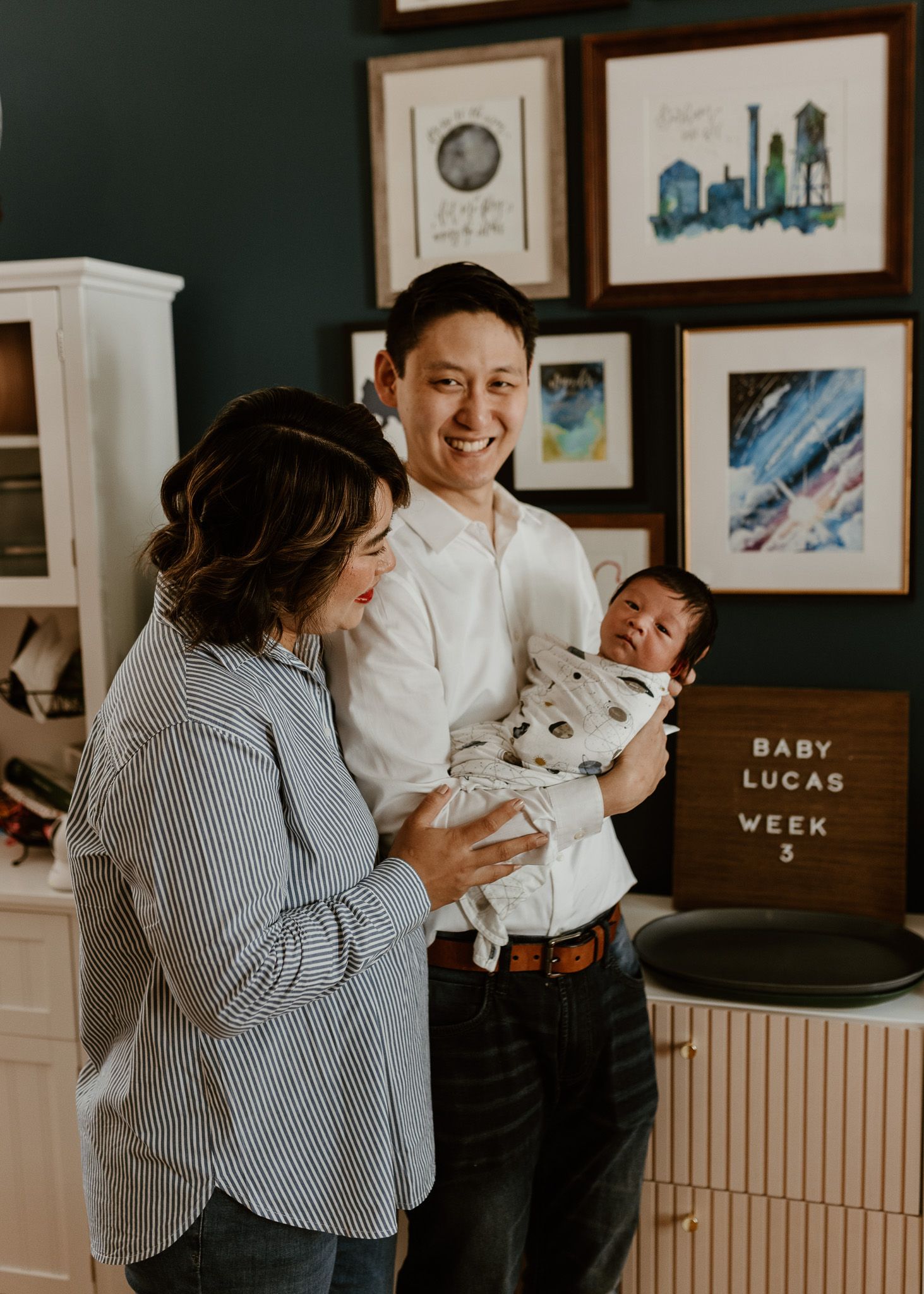 Happy parents smiling and holding their newborn baby Lucas at week 3 in a beautifully decorated nursery room.