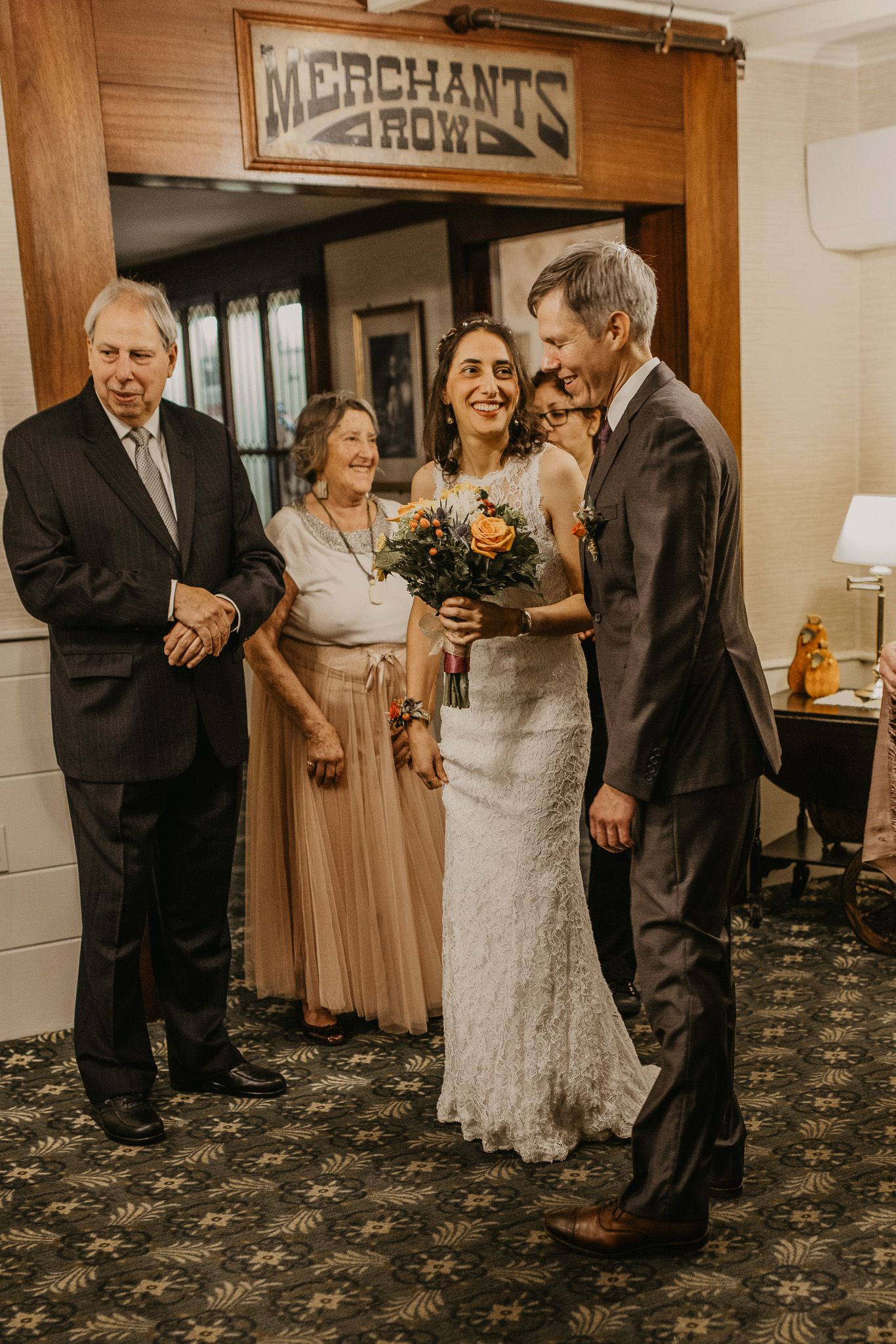 Bride and groom share a joyful moment with family inside a venue under a Merchants Row sign.