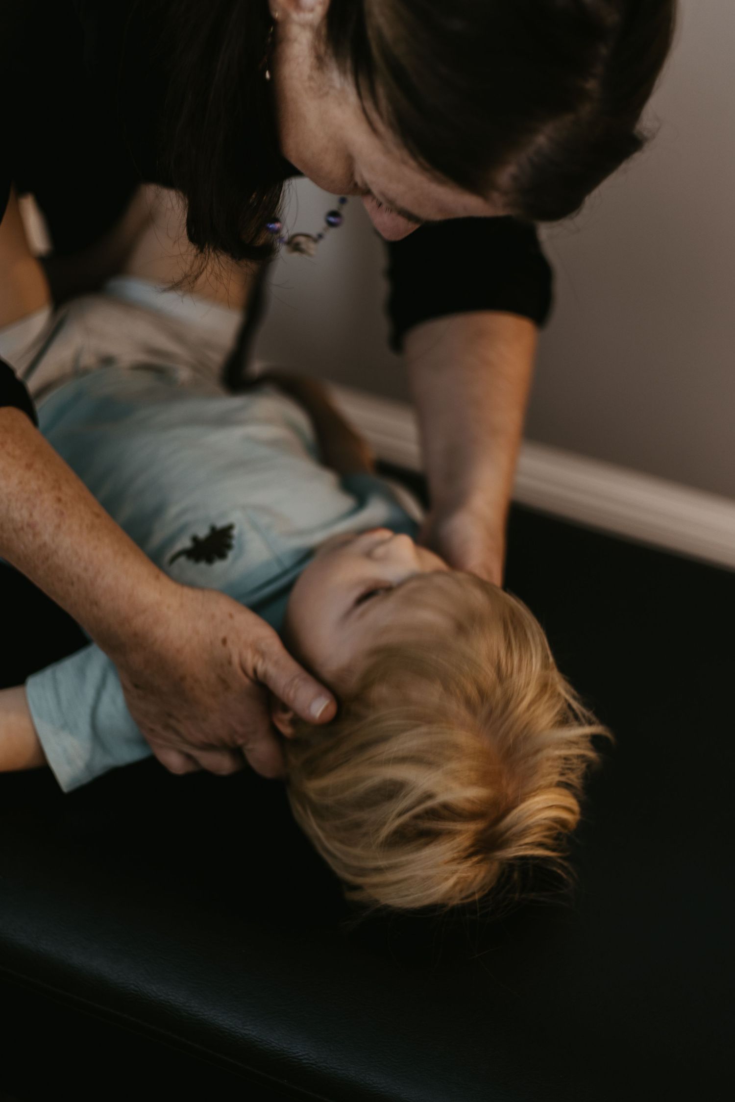 Chiropractor gently adjusting the neck of a young toddler lying on a treatment table during a pediatric chiropractic session.