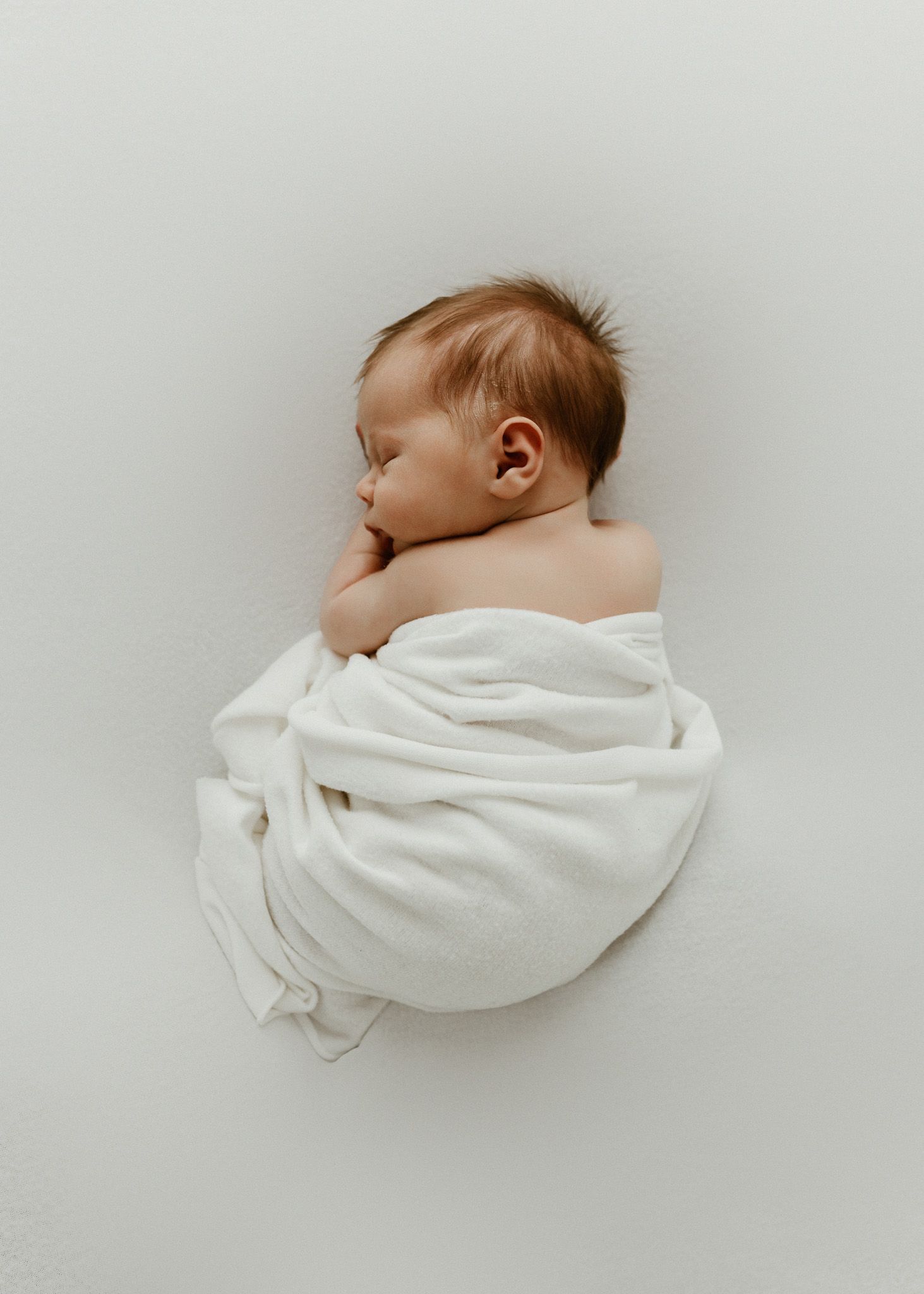 Sleeping newborn baby wrapped in soft white blanket against light background in minimalist style.