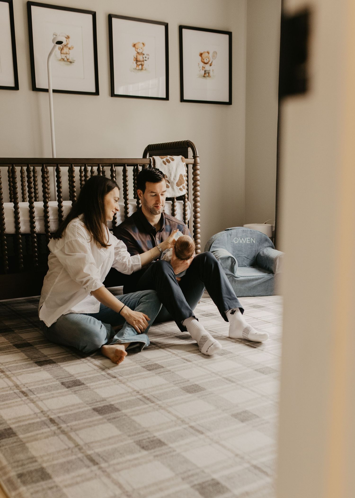 Couple sitting on floor playing with pet in nursery with framed artwork.