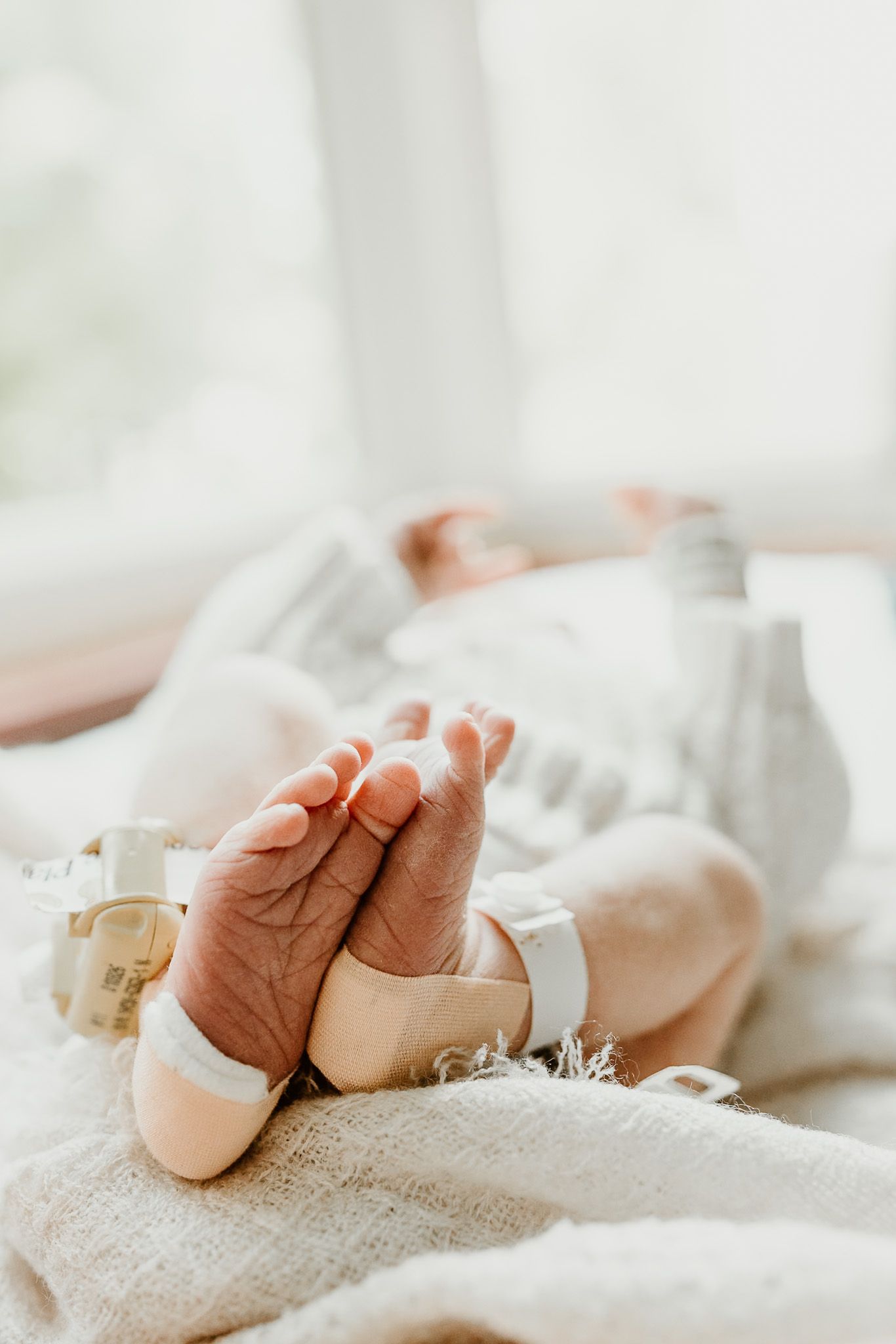 Close-up of newborn baby feet with hospital ID bracelet resting on soft white blanket.