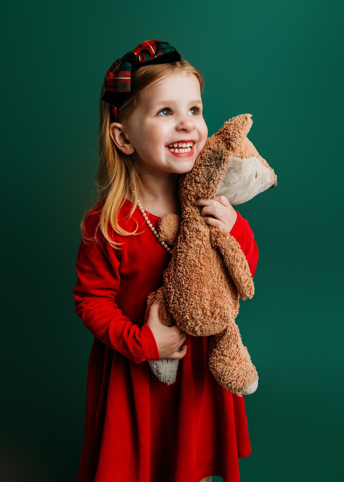 Child in red sweater hugging teddy bear against dark green background.