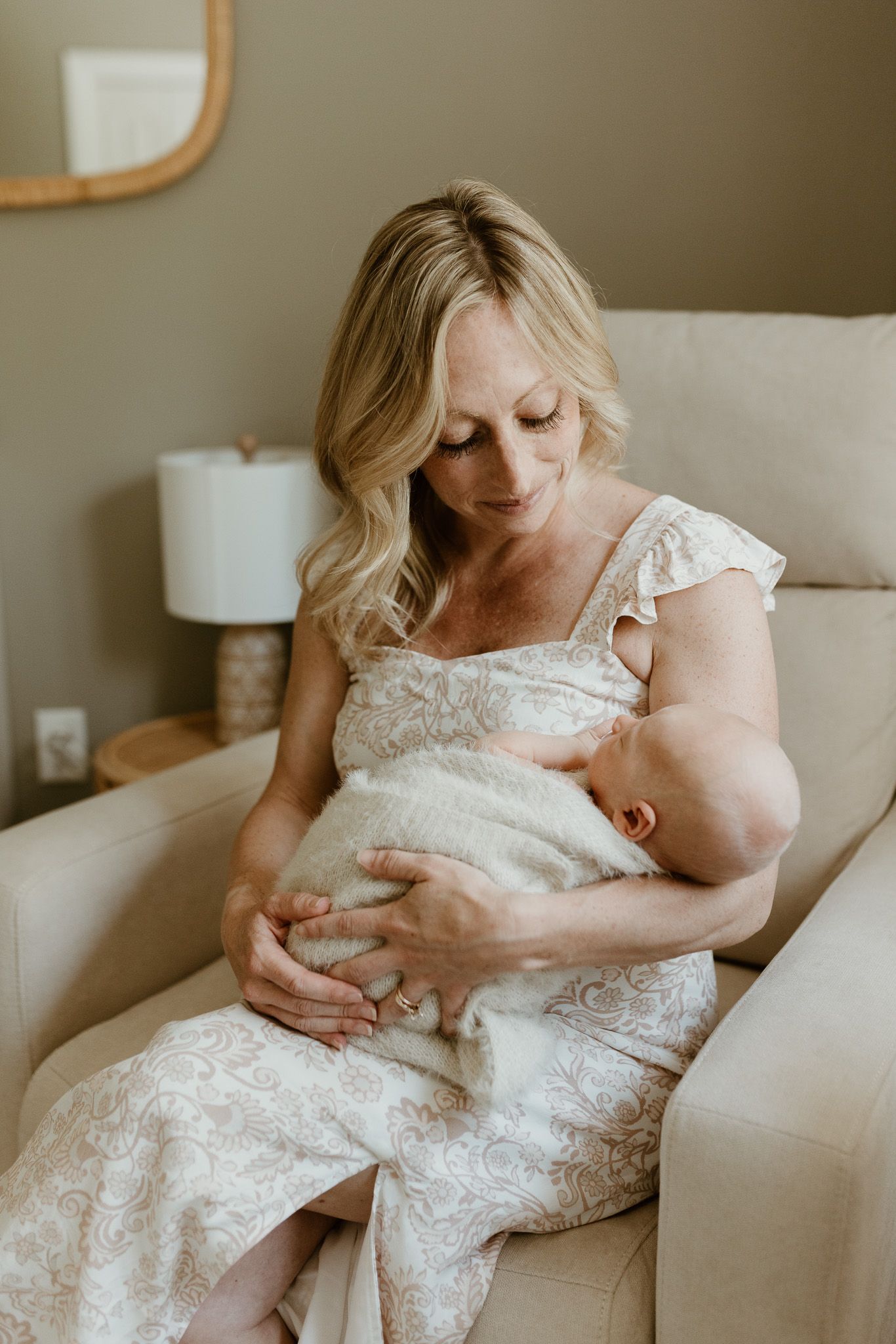 A peaceful moment in a living room as a mother in a white lace dress cradles her sleeping newborn.