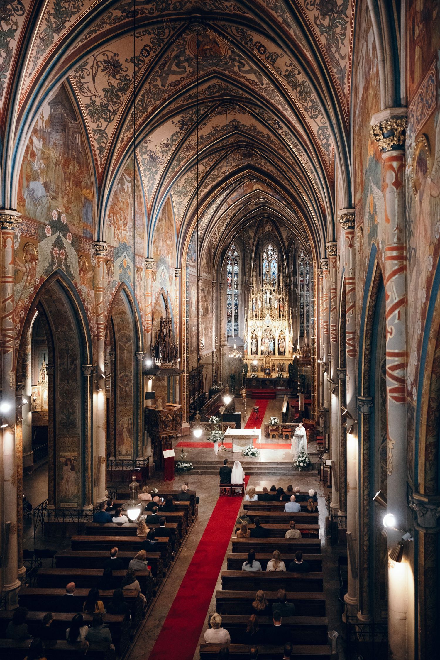 Ornate Gothic church interior with vaulted painted ceilings and red carpet aisle.