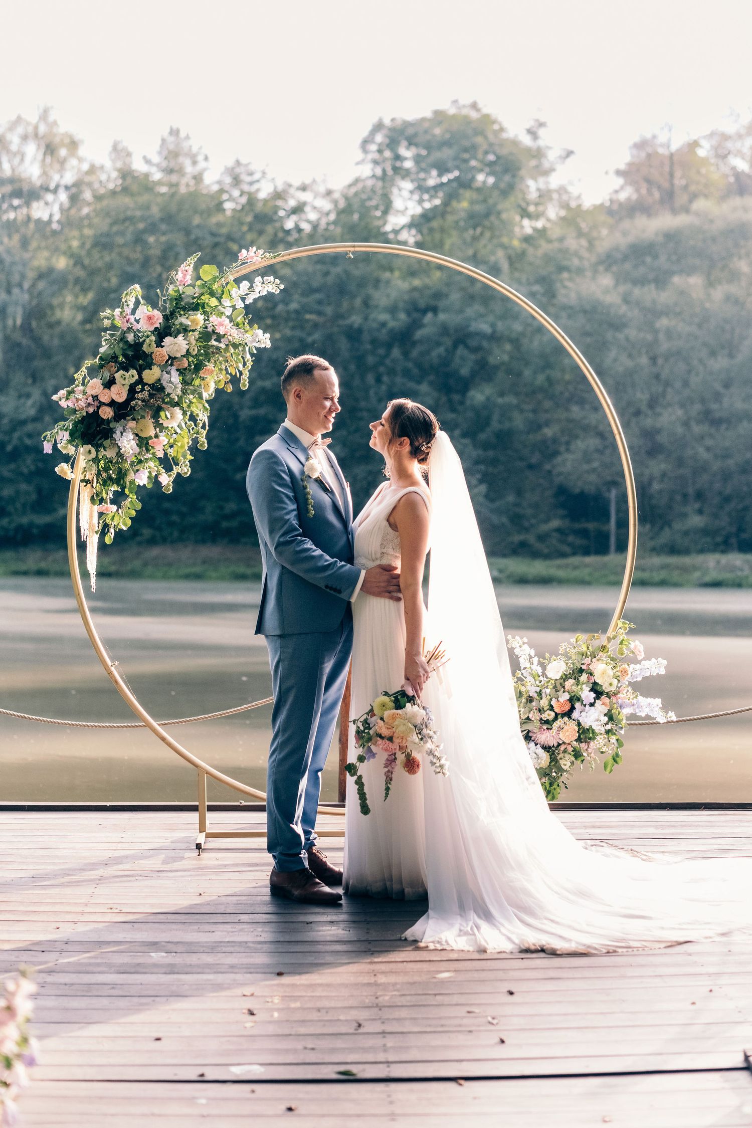 Wedding ceremony under circular arch decorated with fresh flowers on wooden platform.