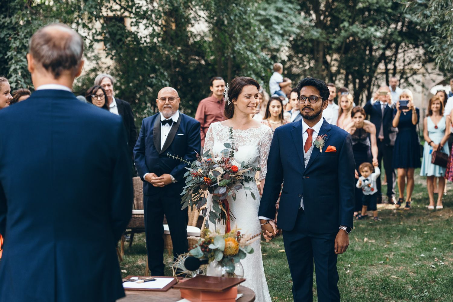Wedding guests and party members gather outdoors for a summer garden ceremony.