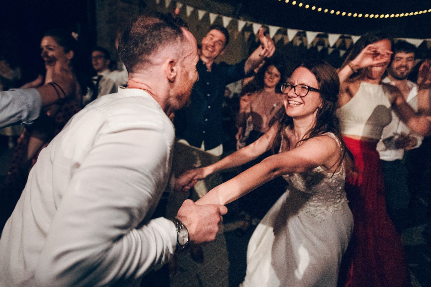 Dancing and celebration at a wedding reception with string lights and bunting.