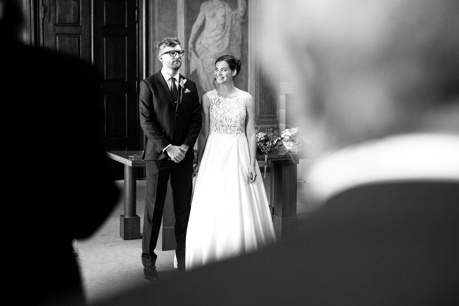 Black and white wedding photograph in an elegant indoor venue with arched doorways.