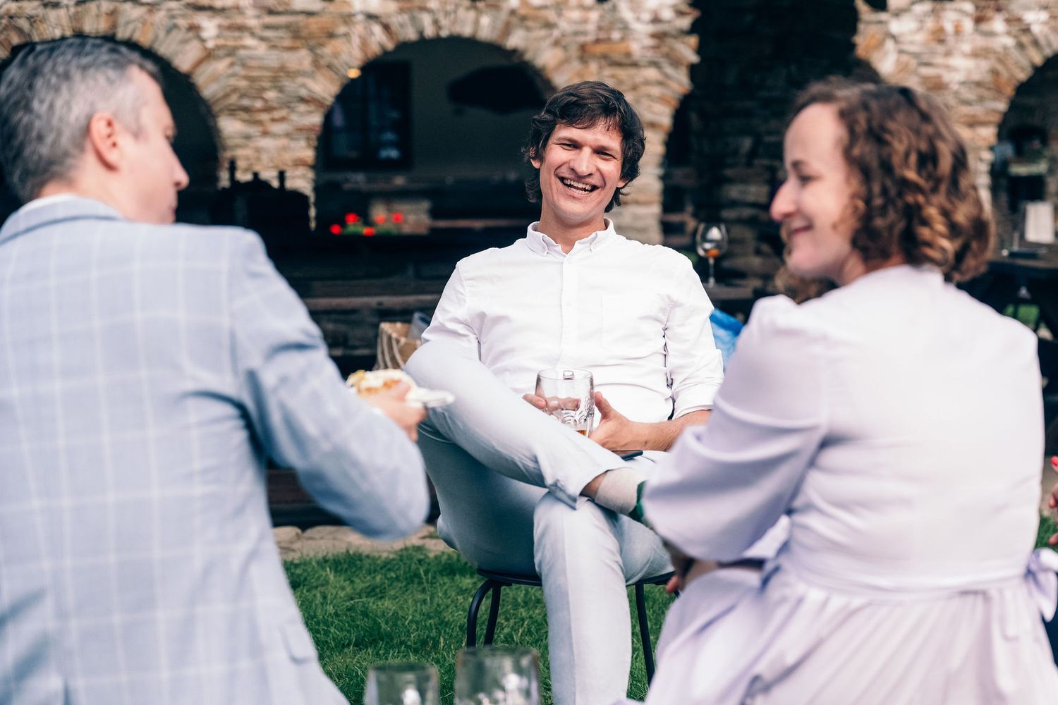 Wedding party relaxing and laughing together against stone wall backdrop.