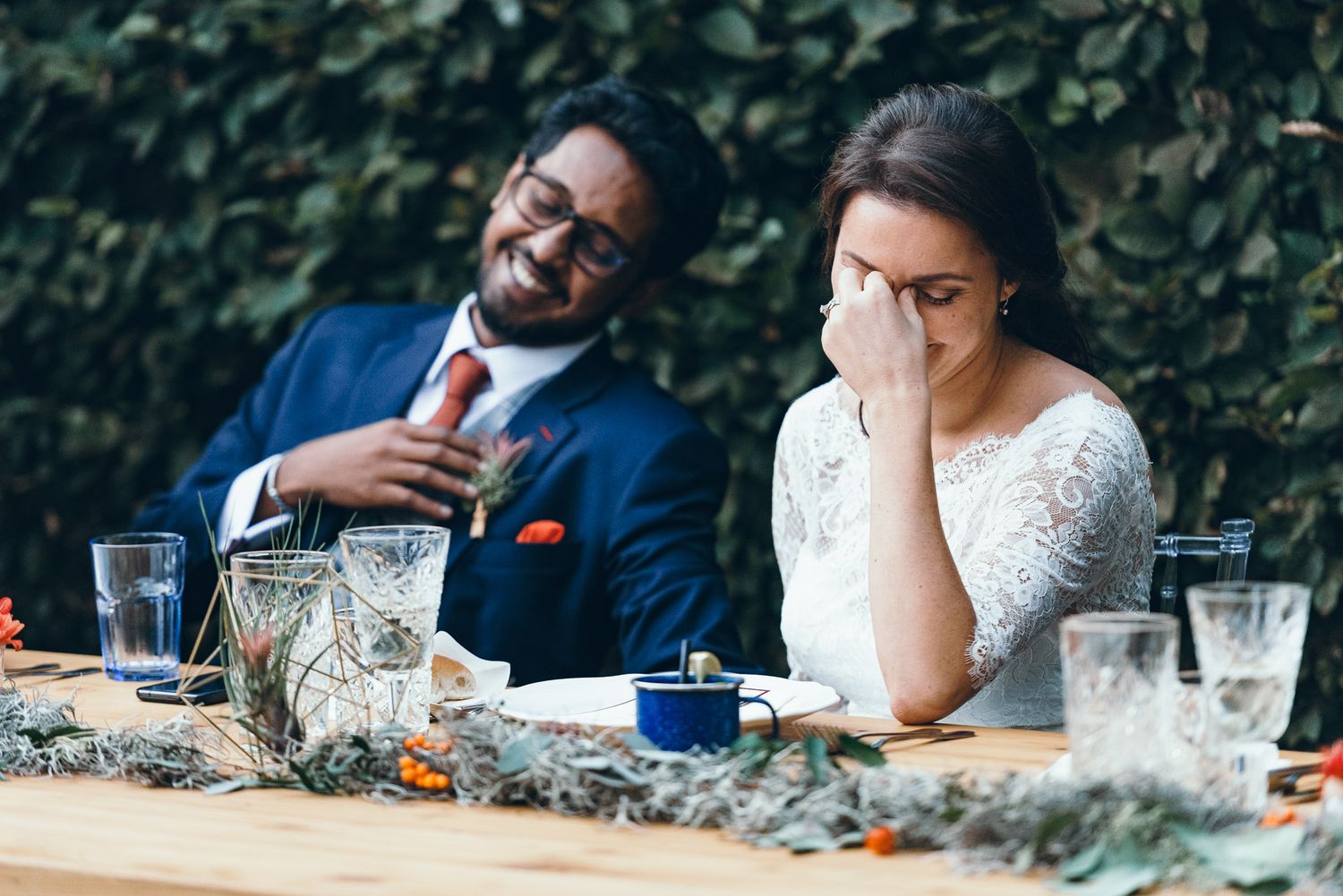 A couple shares a candid moment at an outdoor wedding reception table with drinks and decor.