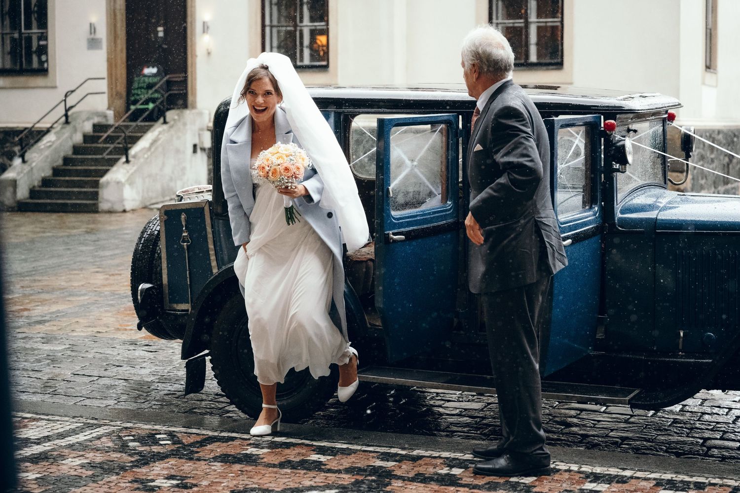A classic vintage car on a rainy day being used for wedding transportation.