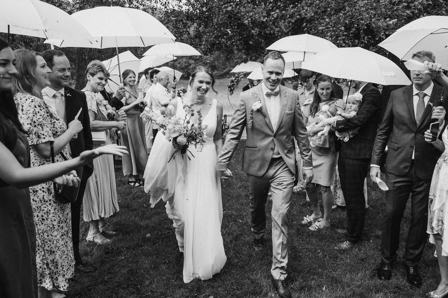 Wedding guests holding white umbrellas while walking through a garden.
