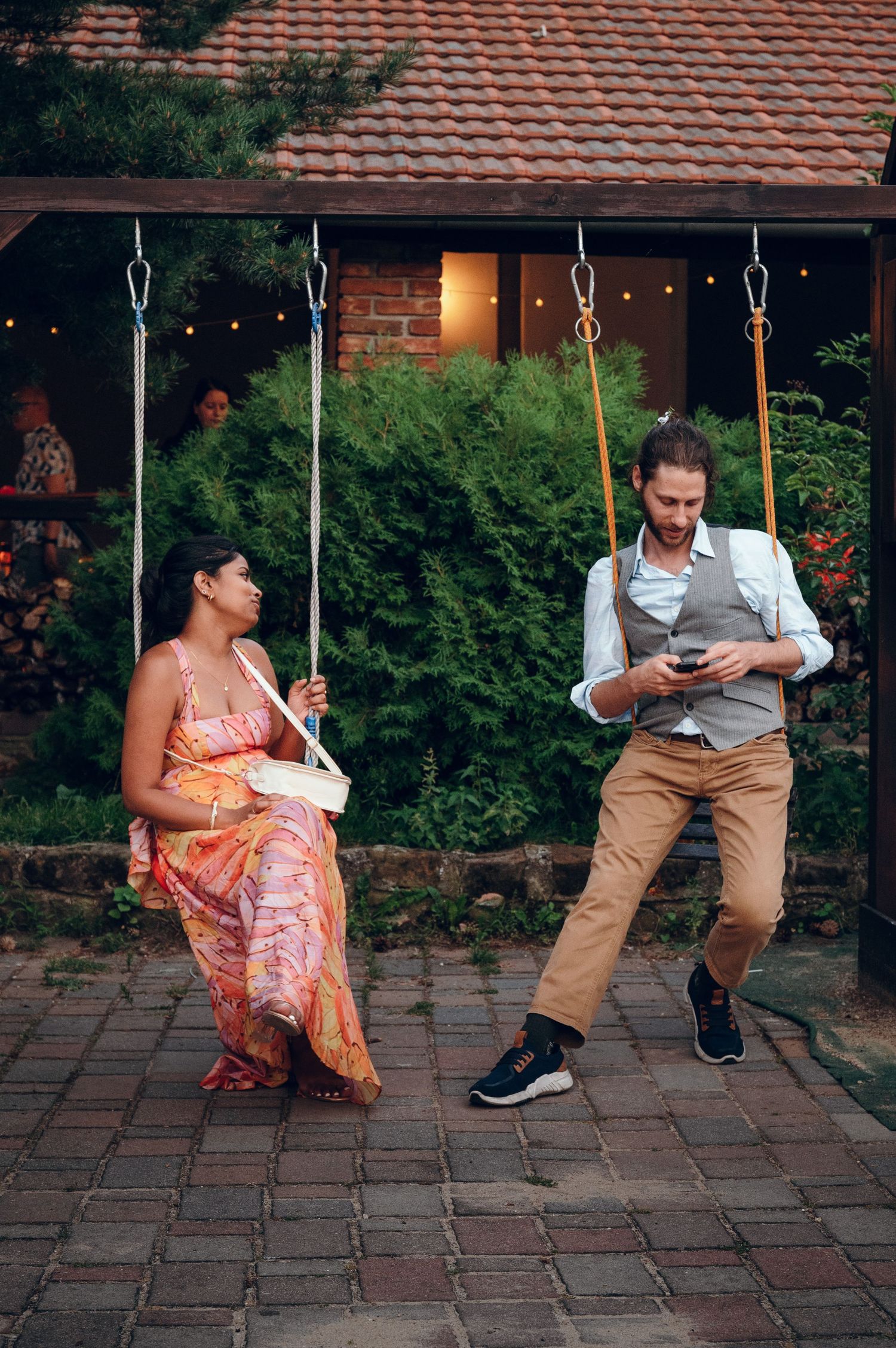 Wedding guests having fun on playground swings in formal attire.