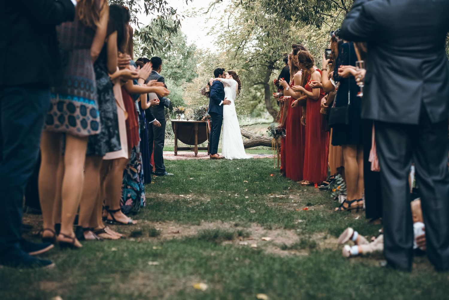 Wedding guests toss red flower petals during an outdoor garden ceremony celebration.