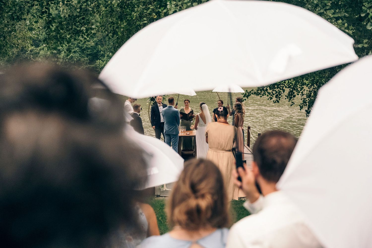 Outdoor wedding ceremony scene with white umbrellas and guests on a sunny day.