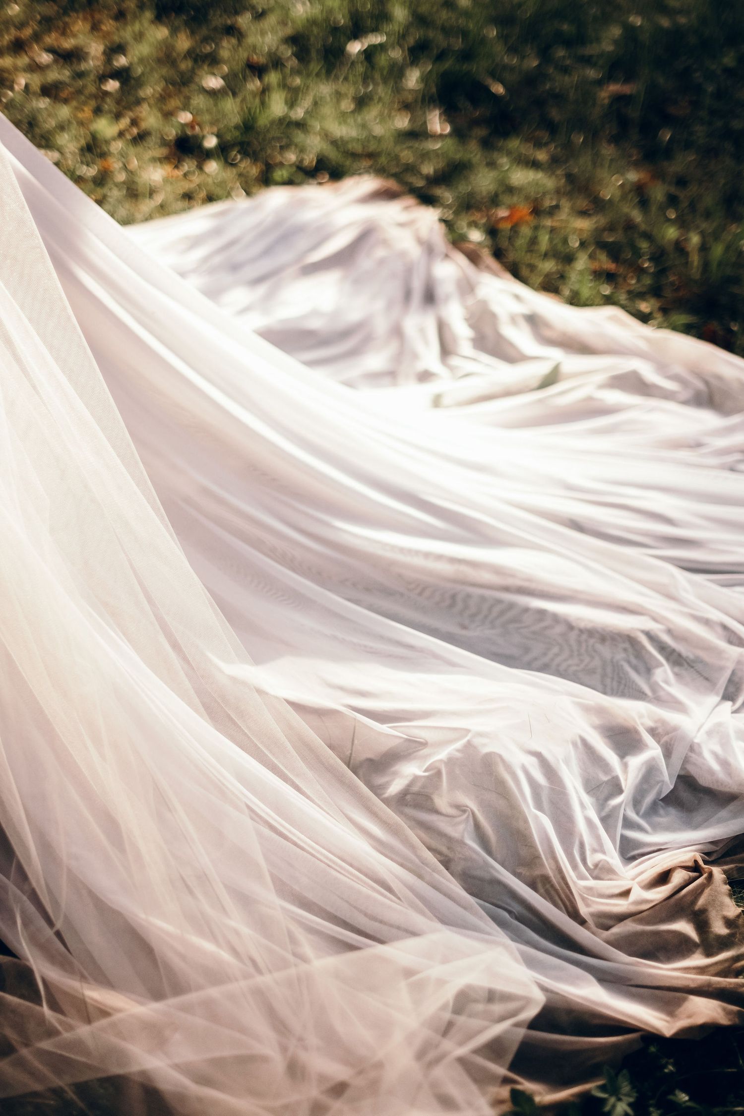Flowing white wedding veil dramatically spread across a natural outdoor setting.
