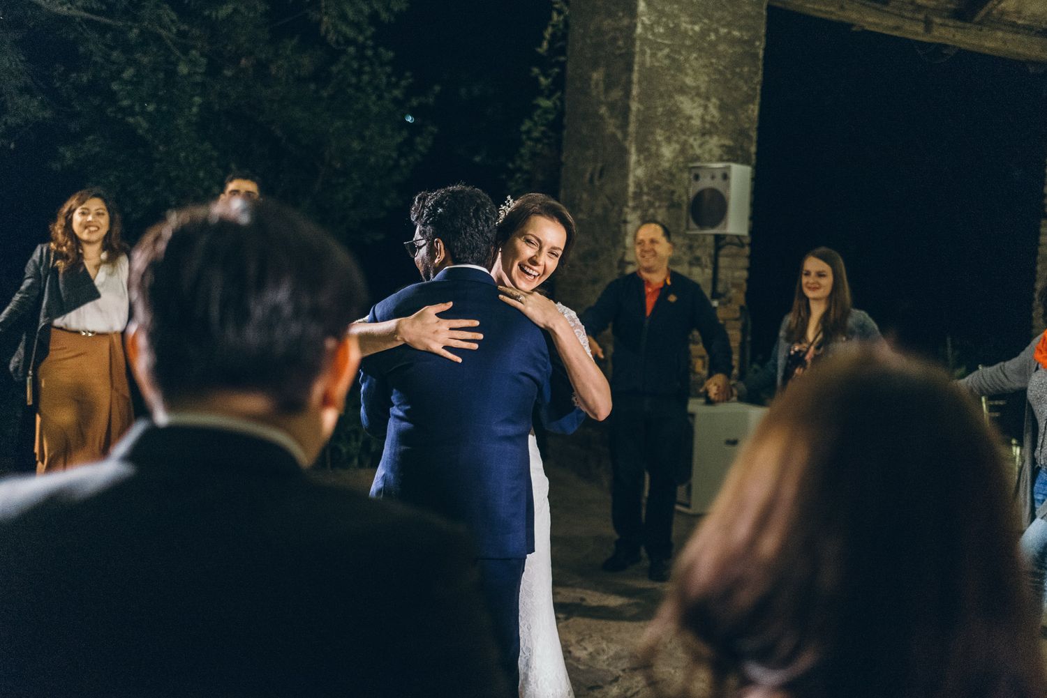 Two people embrace during a wedding celebration as guests watch.
