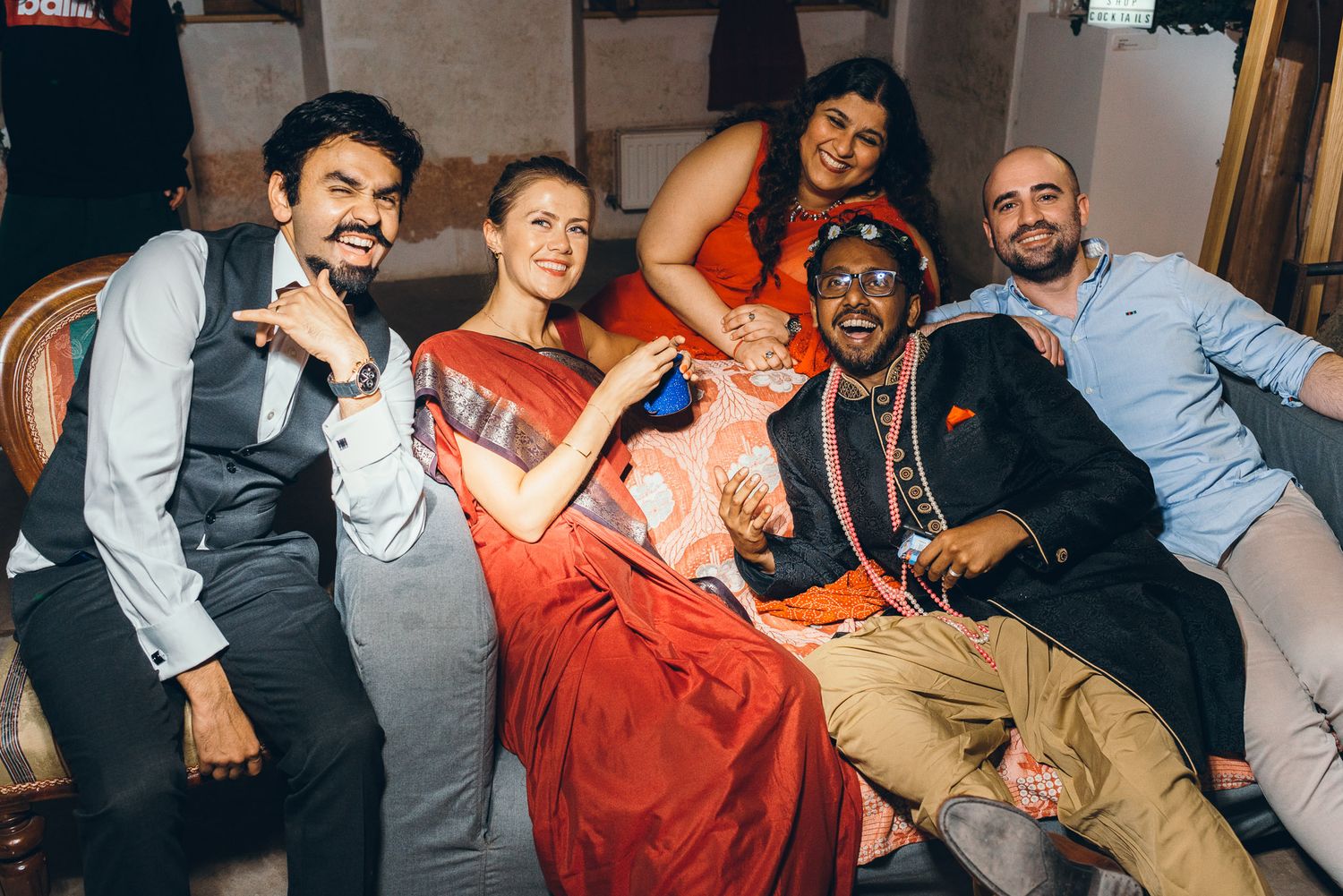 A group of wedding guests pose together on a couch at a reception celebration.