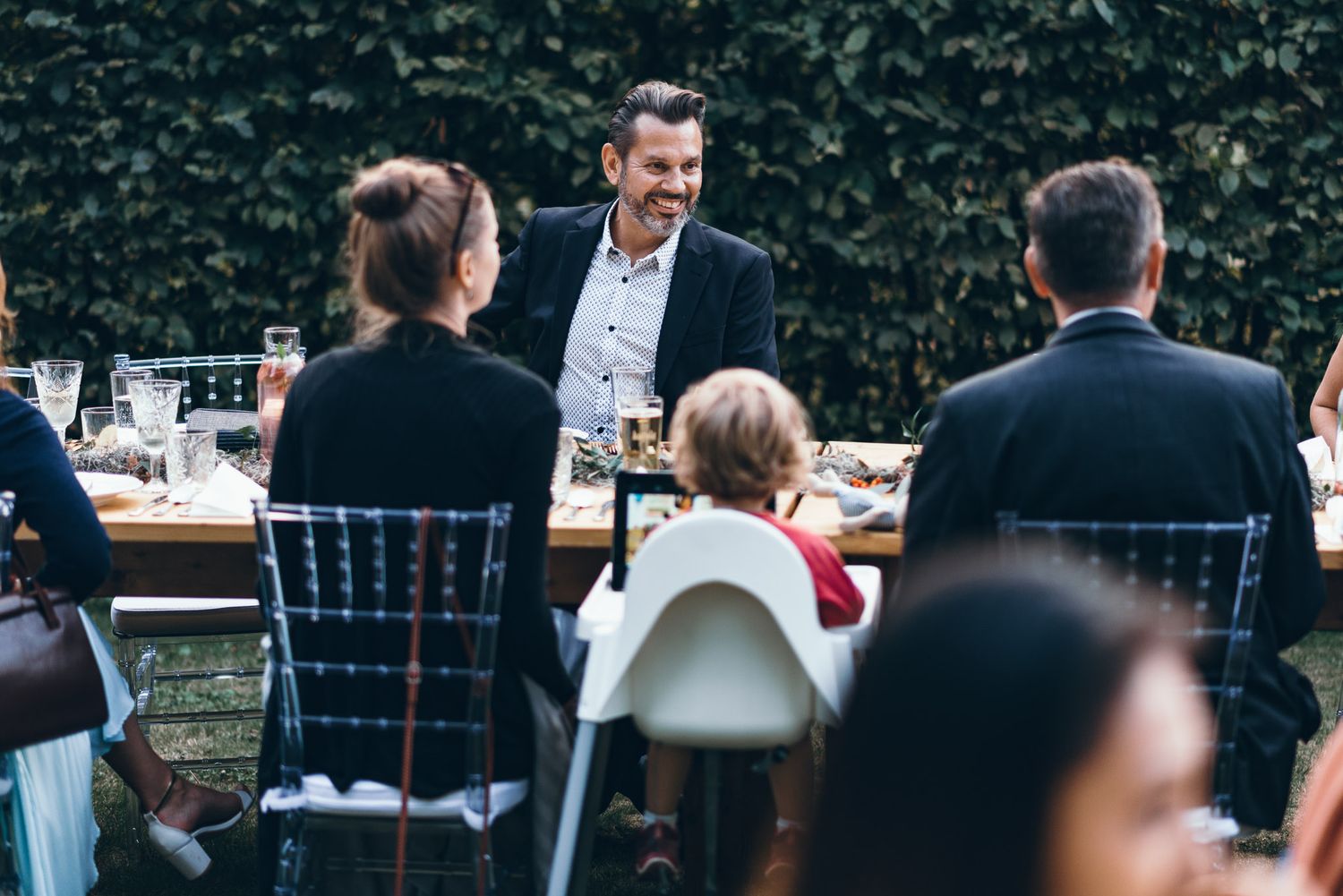 Wedding reception dinner setup with elegant table settings and hedge wall backdrop.