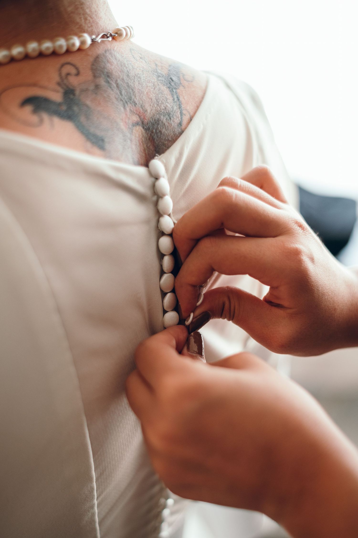 Detailed shot of pearl buttons being fastened on a white wedding dress.
