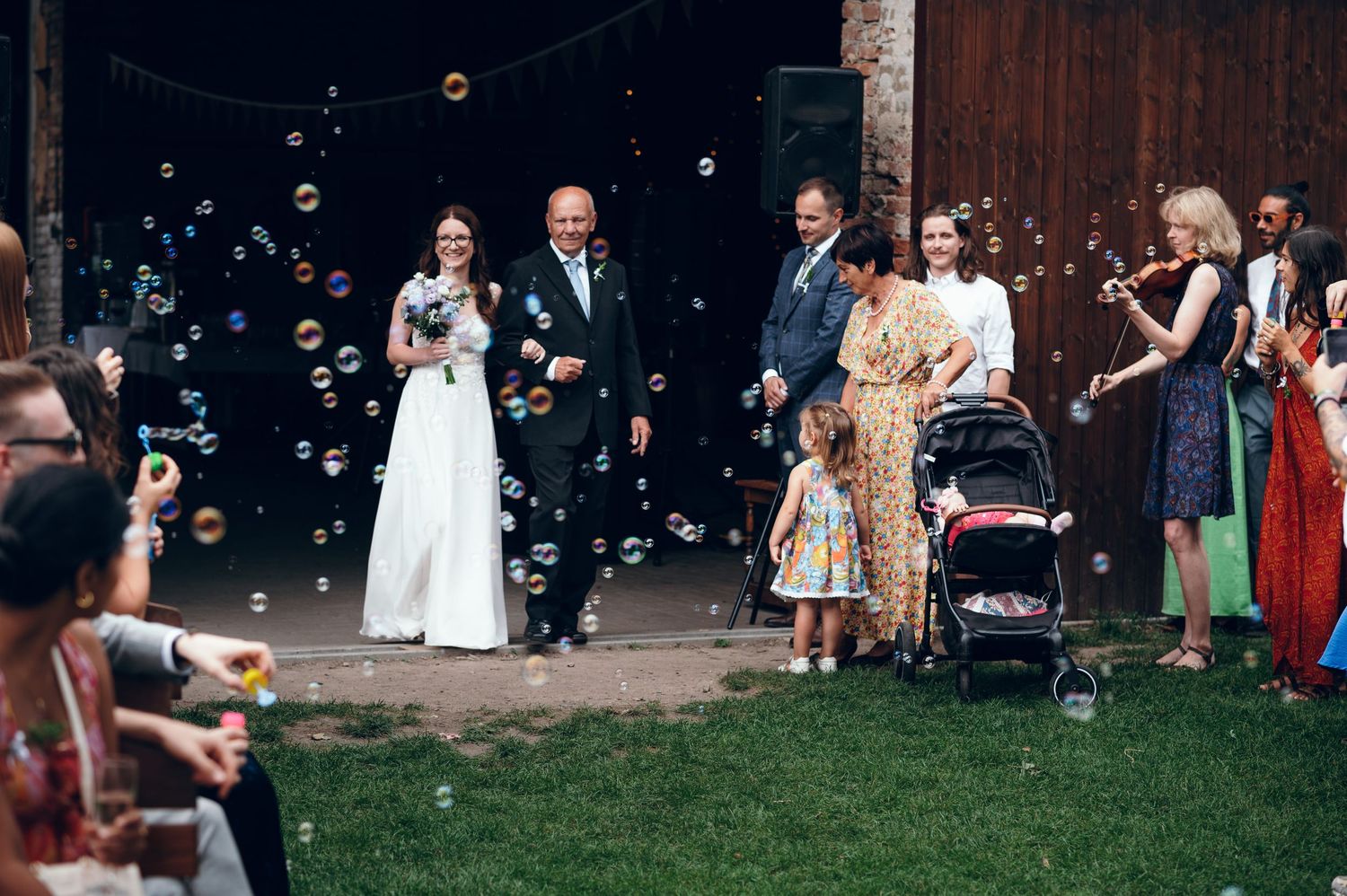 Wedding guests gather outdoors while soap bubbles float through the air.