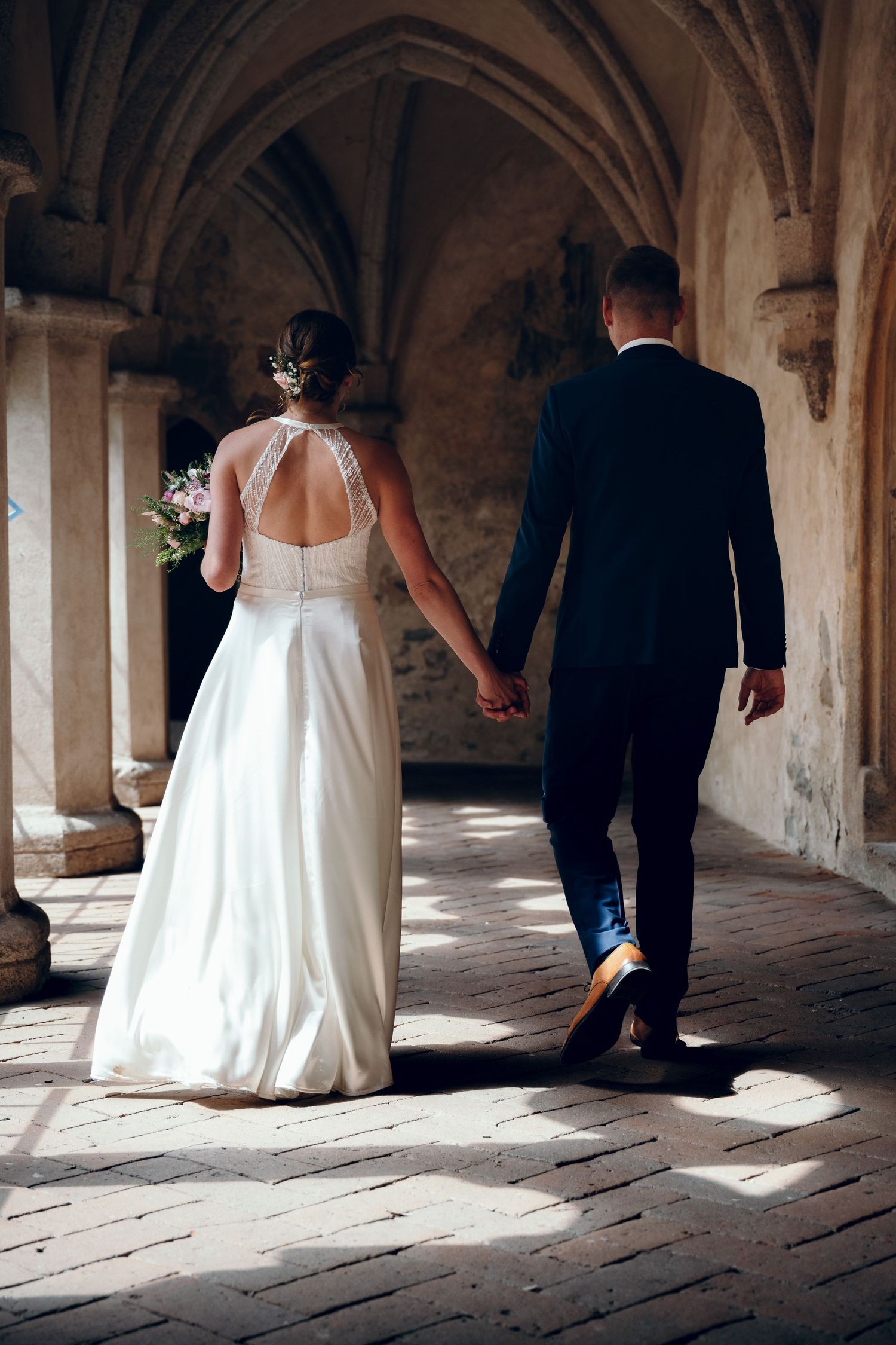 Artistic black and white shot of wedding attire in a stone archway corridor.
