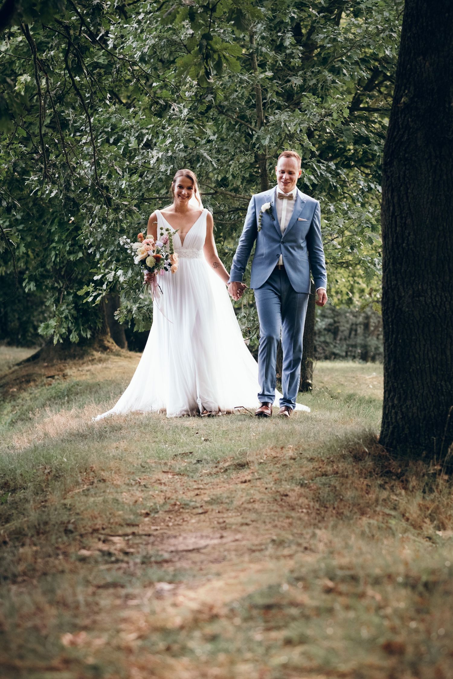 A couple walking through a wooded area during their wedding photoshoot.
