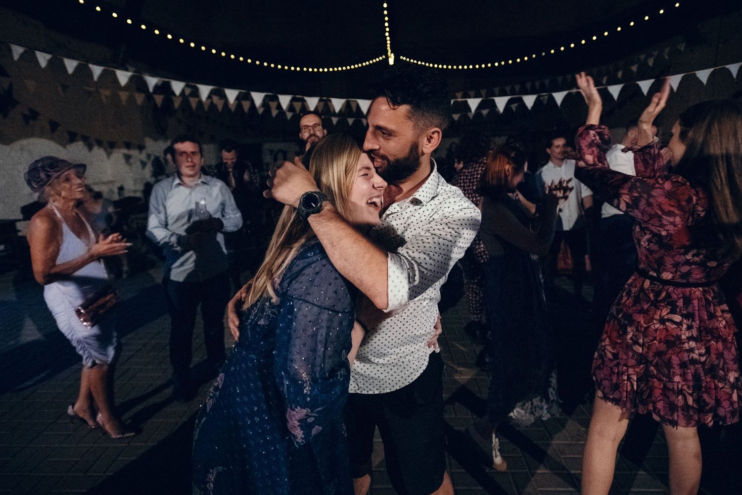 Wedding reception dance floor filled with guests dancing under string lights and bunting.