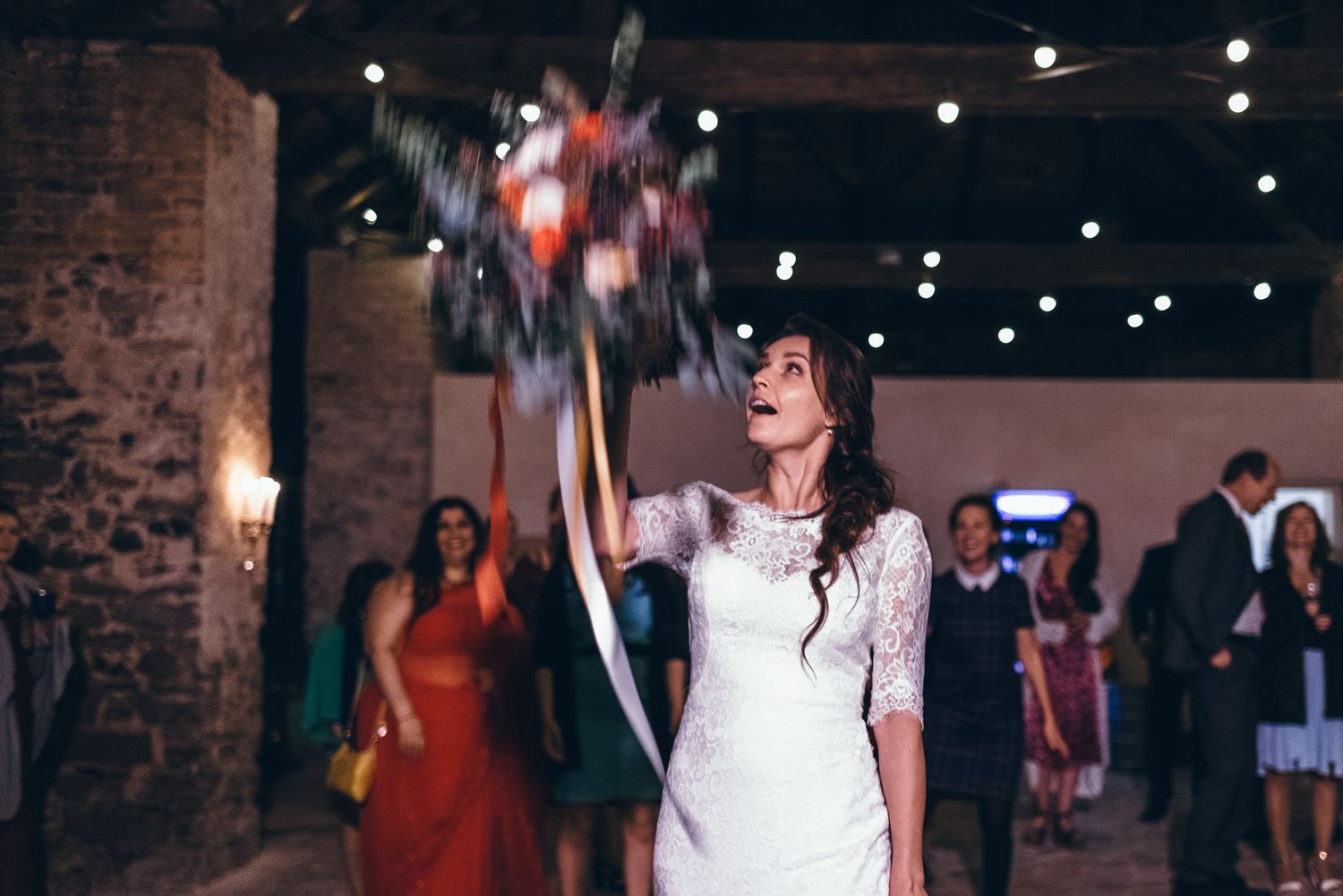 A person in a white lace dress tosses a bouquet during a wedding reception.
