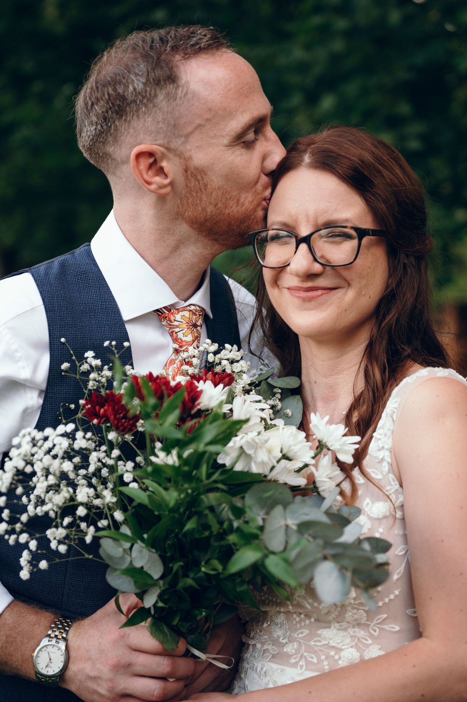 Close up of wedding couple with white and burgundy floral bouquet.