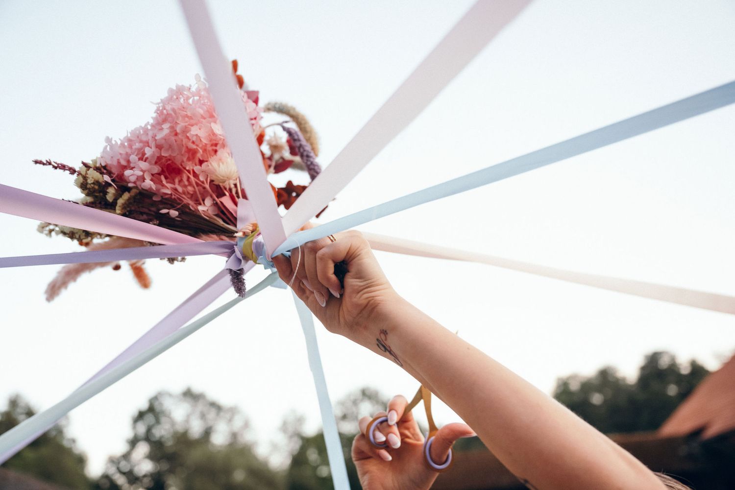Close-up of hands attaching pink floral decorations to a white wedding arch.