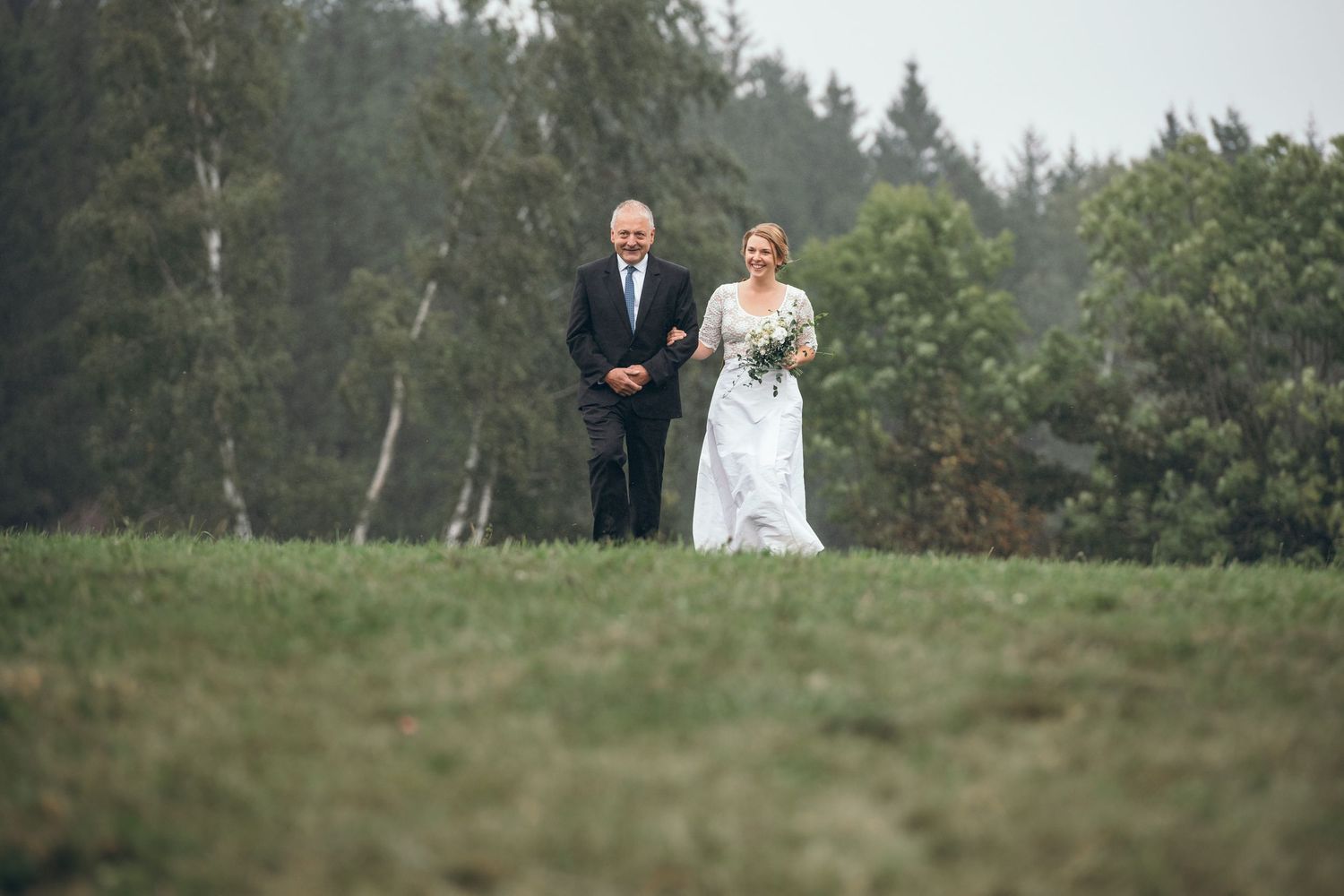Couple walking together on a grassy hillside during an outdoor wedding ceremony.