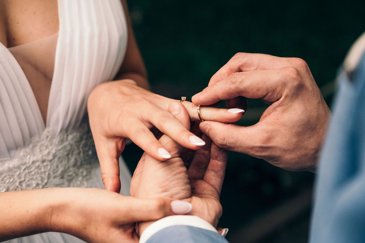 Close-up of hands exchanging wedding rings during outdoor ceremony.