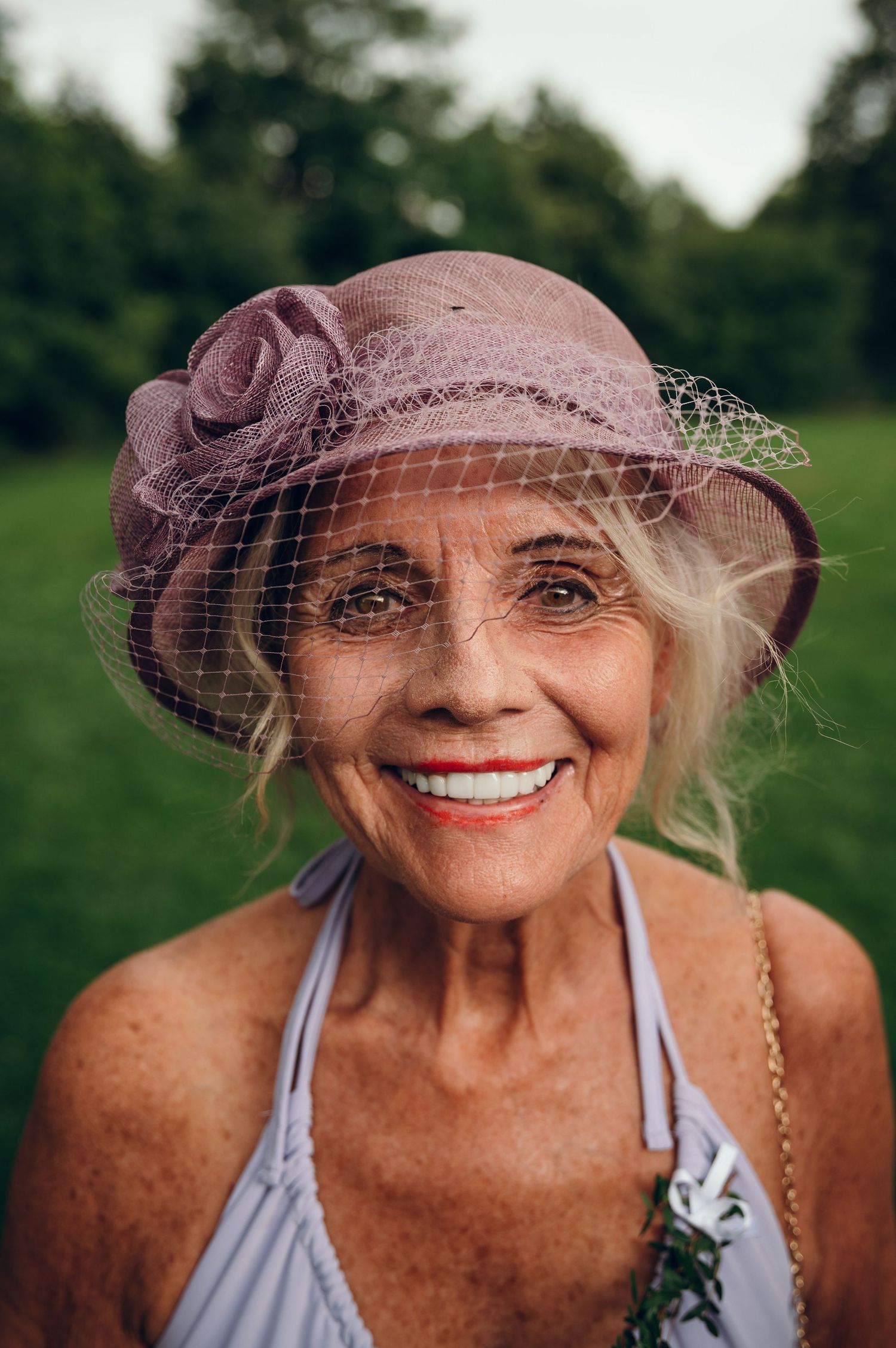 Elegant woman wearing a vintage-style mauve hat with netting against a green outdoor background.