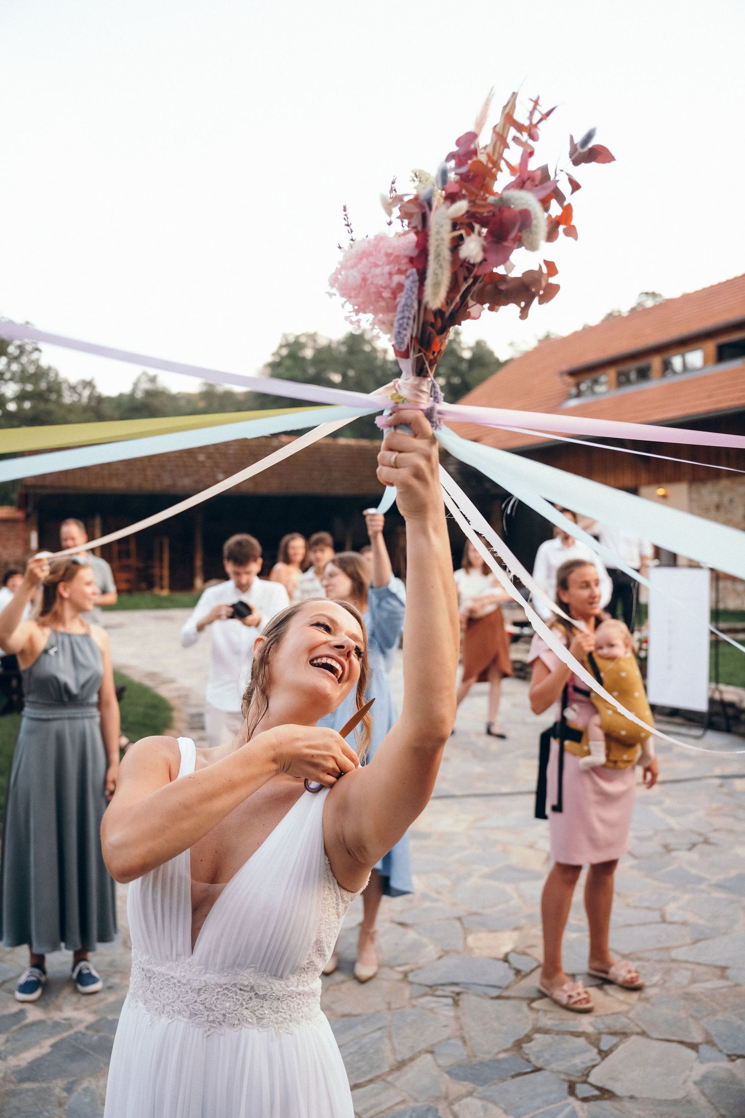Wedding party celebrating on a stone patio with raised bouquets at sunset.