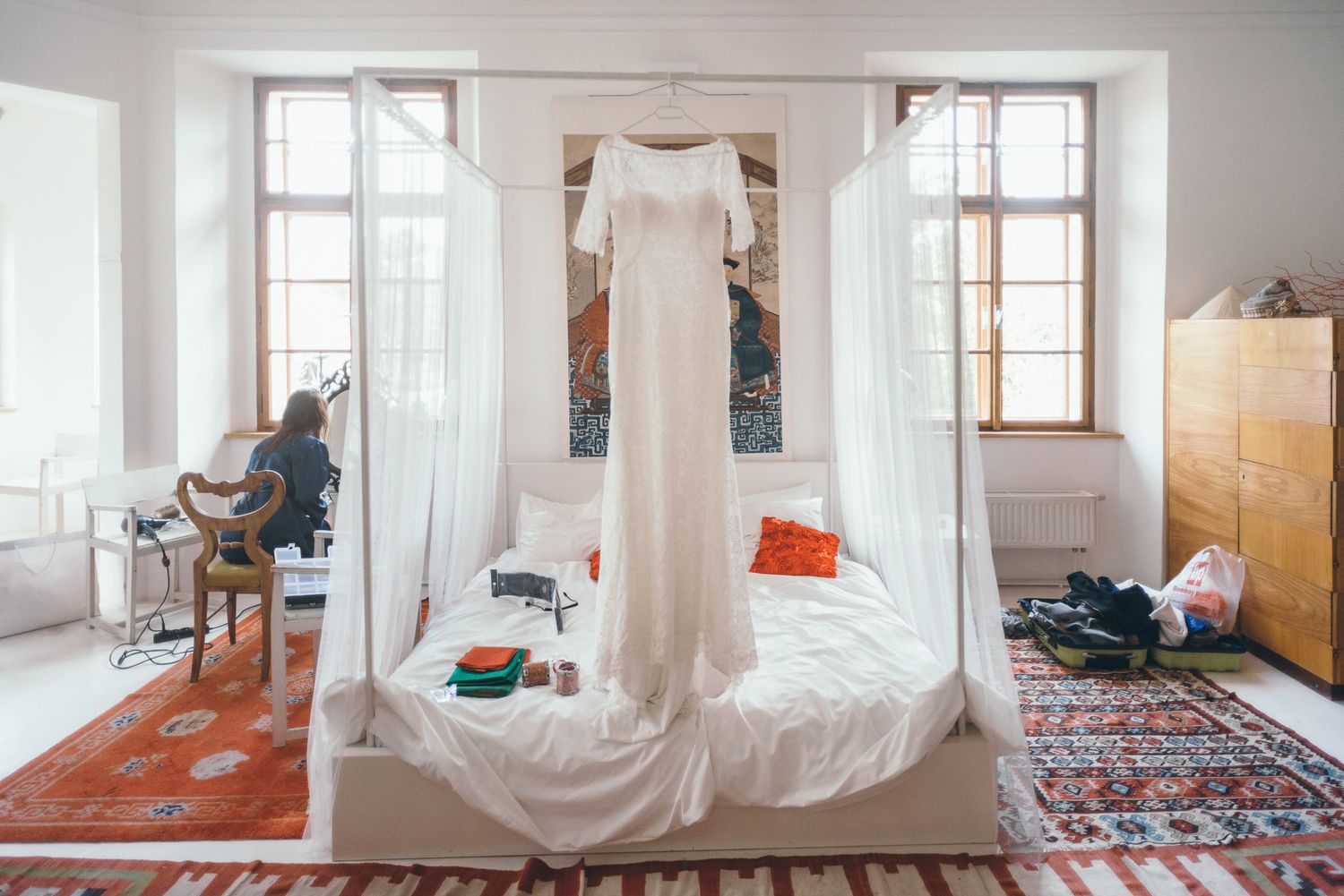 A bright, minimalist white room with large windows and scattered rugs on the wooden floor.