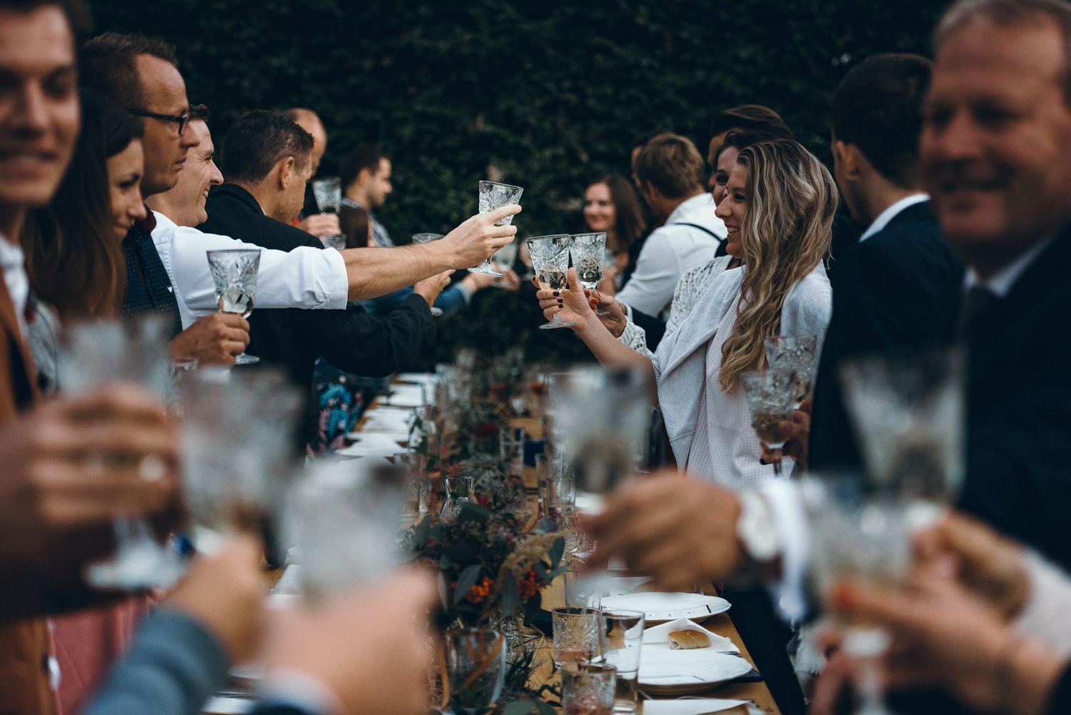 Wedding guests raising glasses for a toast at a long reception table.