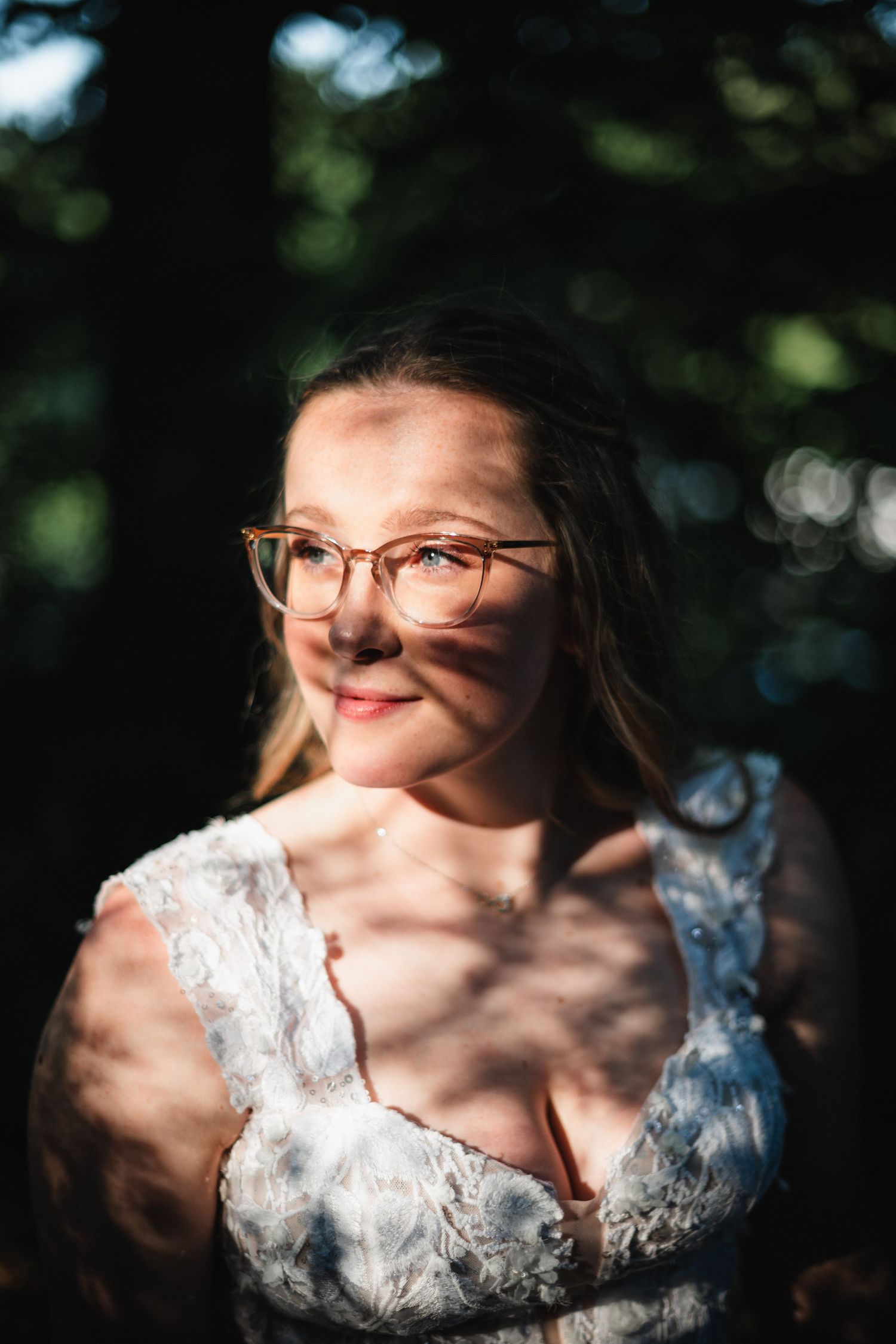 Artistic portrait of someone in white lace wedding attire with dappled sunlight creating shadows.
