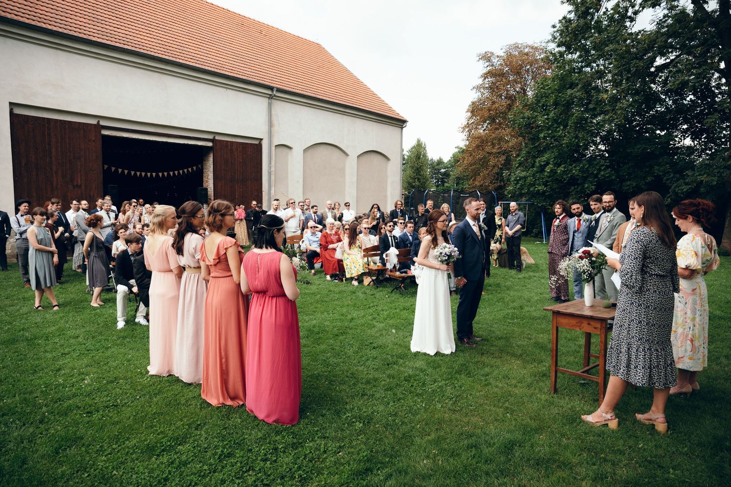 Large group of wedding guests gathered on a grassy lawn outside a brick building.