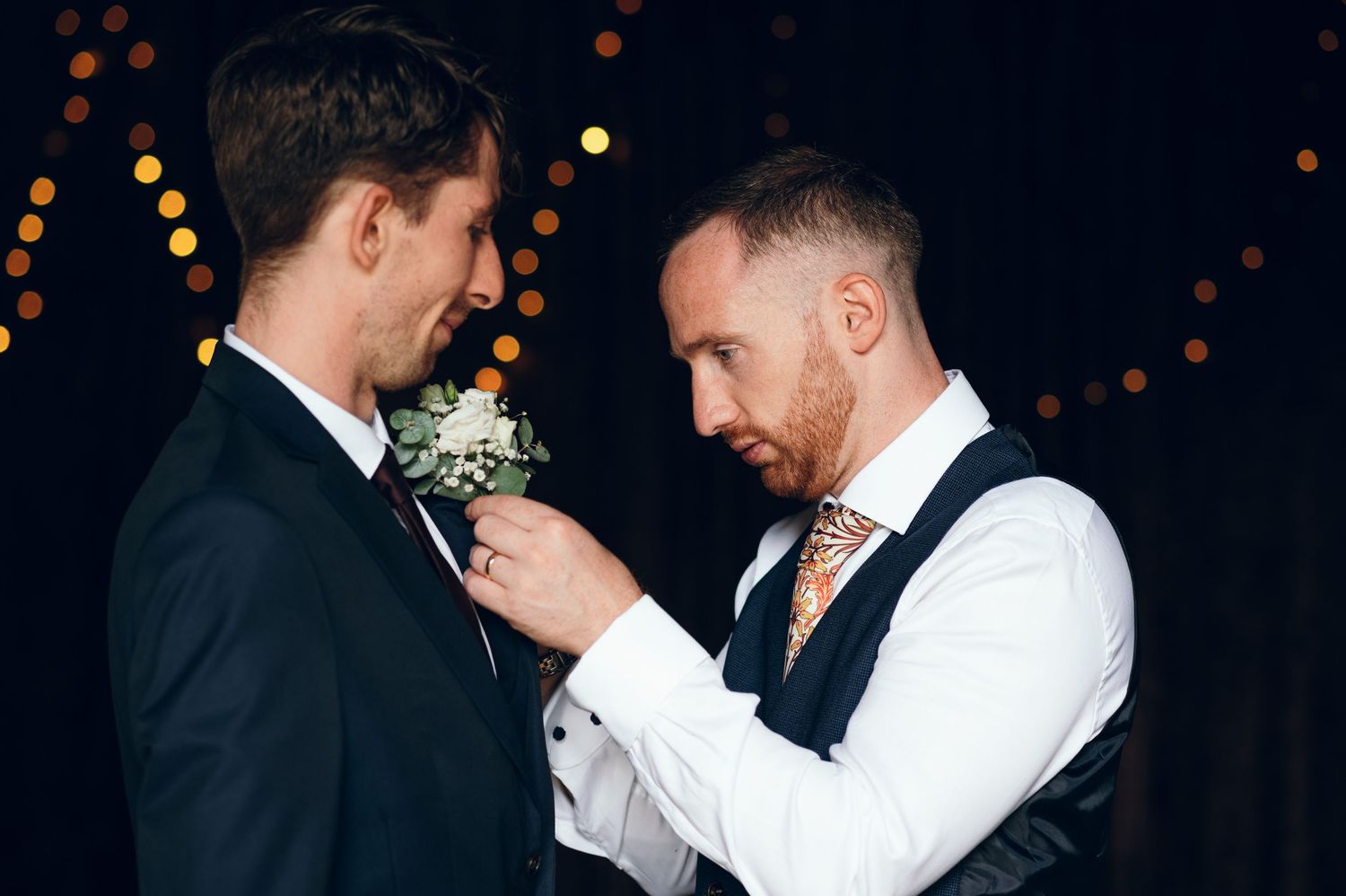Emotional embrace between wedding party members during evening reception with bokeh lights.