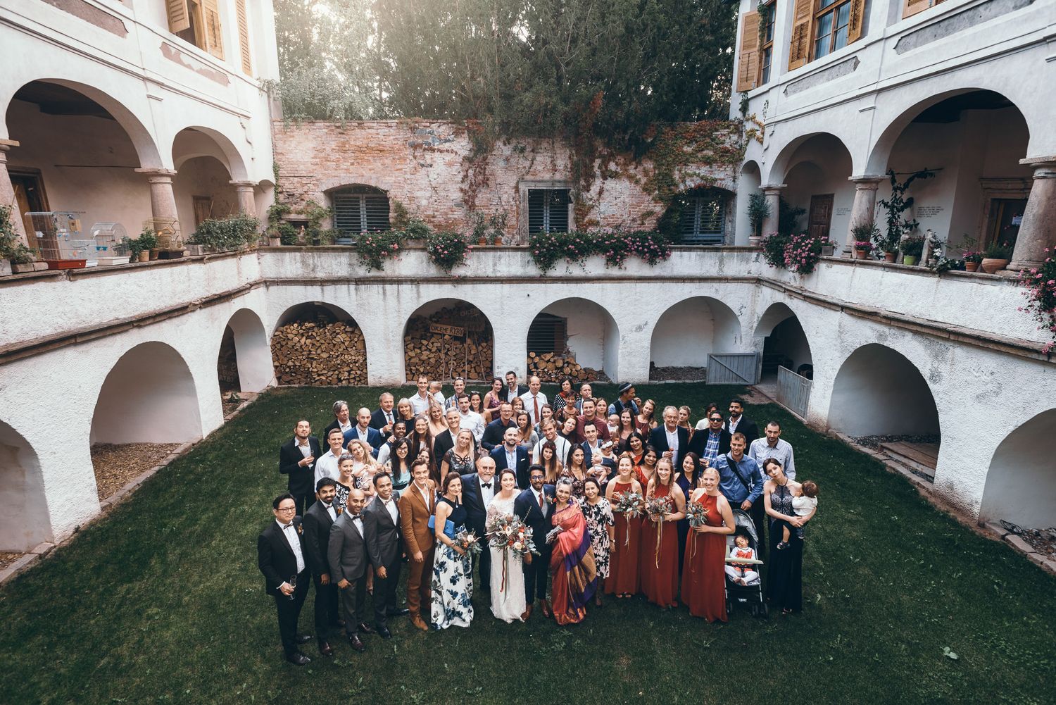 Panoramic view of wedding guests gathered in a historic courtyard with arched architecture.