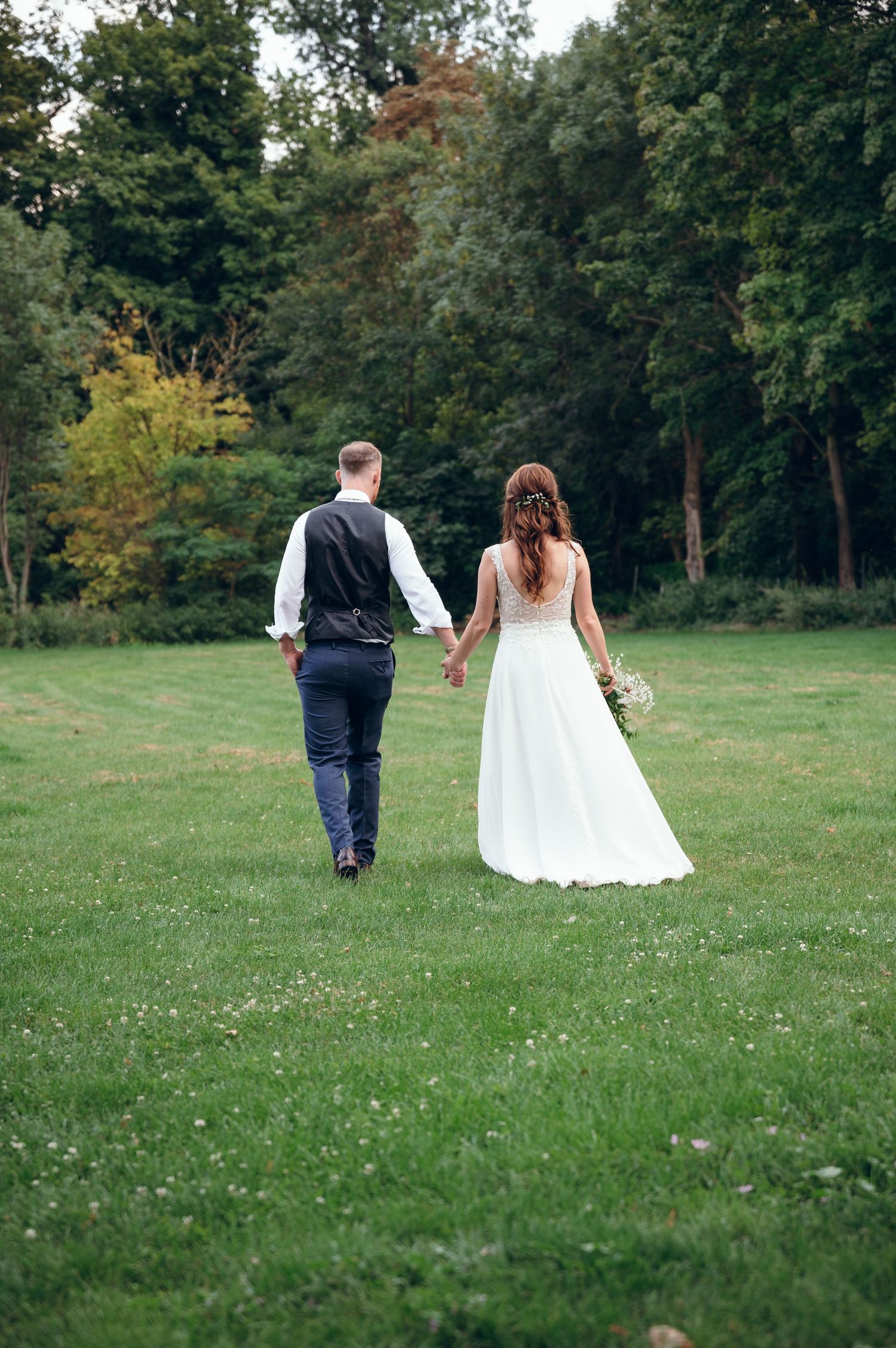 Couple walks away across grassy field during wedding celebration.