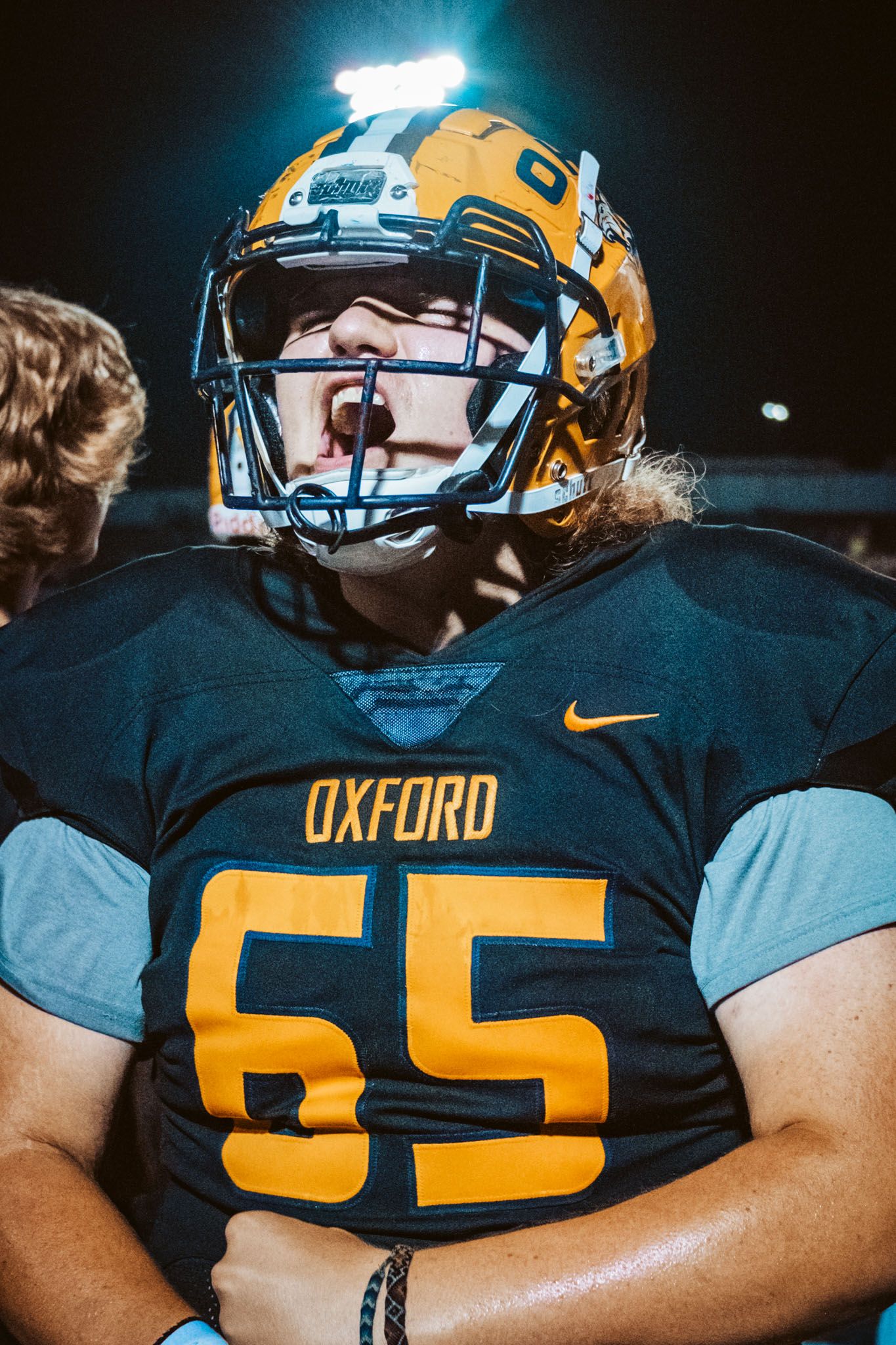 Football players in Oxford navy and gold uniforms lined up on field at night.