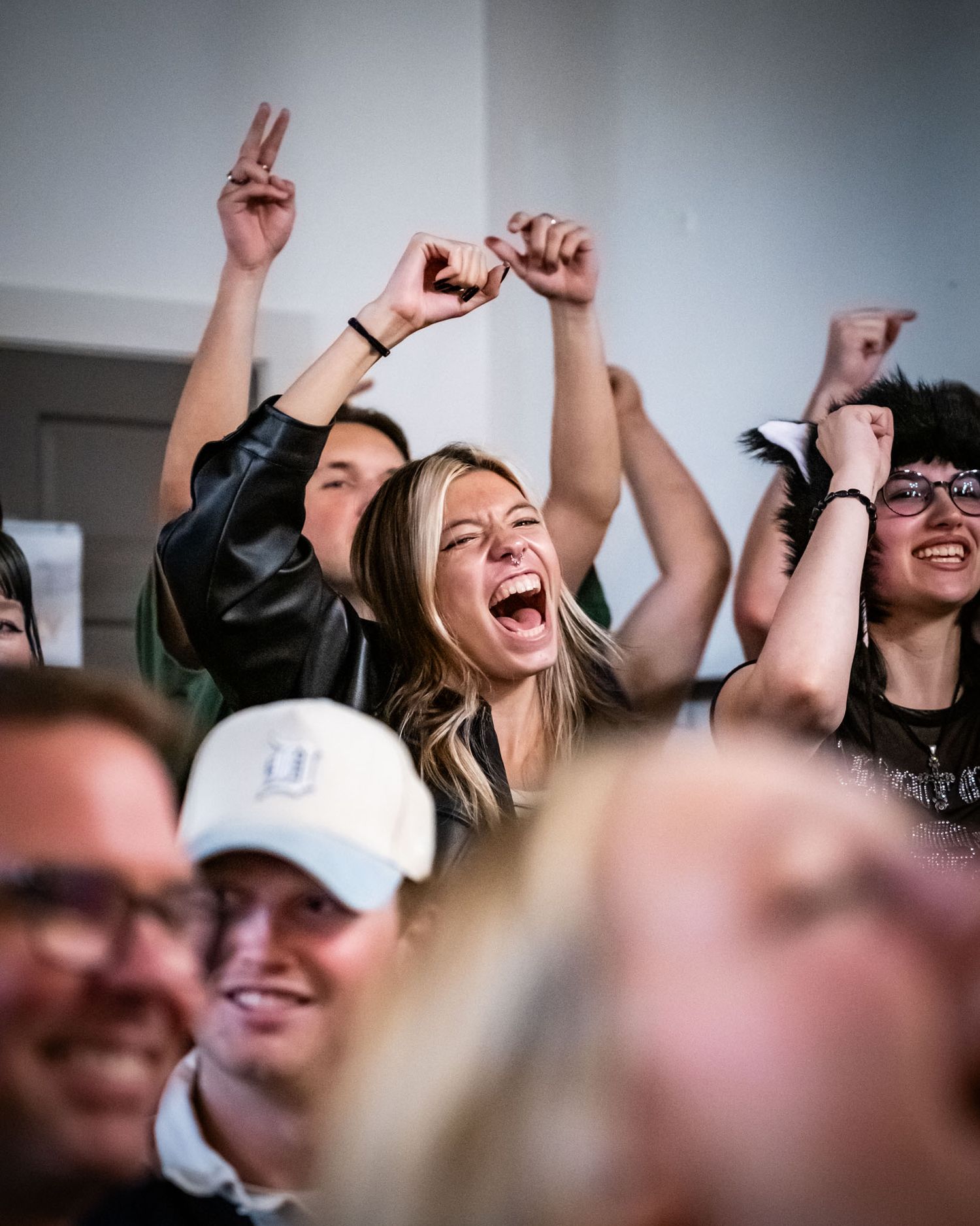 Excited crowd cheering with raised arms at indoor sporting event.
