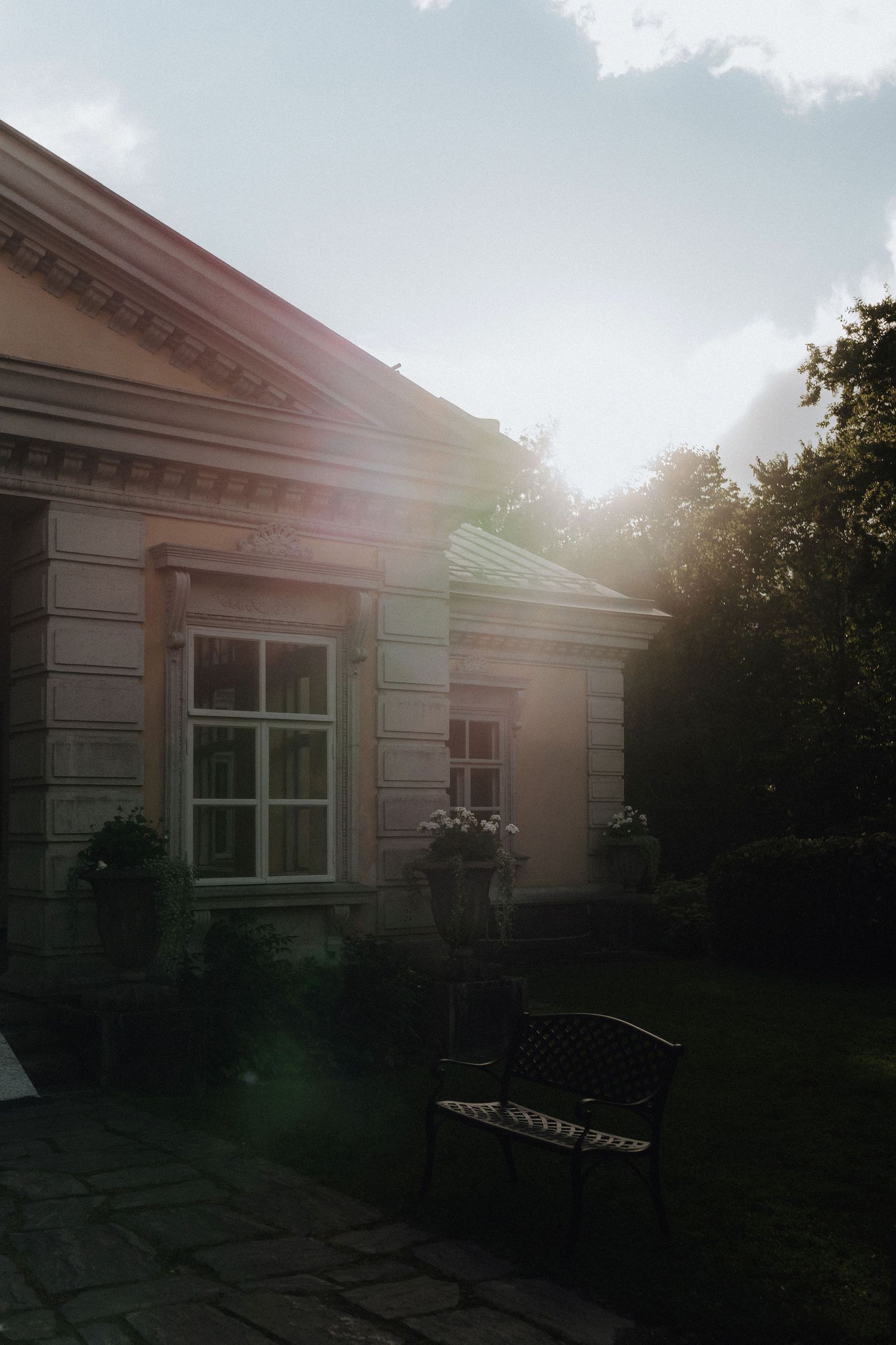Golden sunlight streaming over a classic manor house exterior with a garden bench nearby.